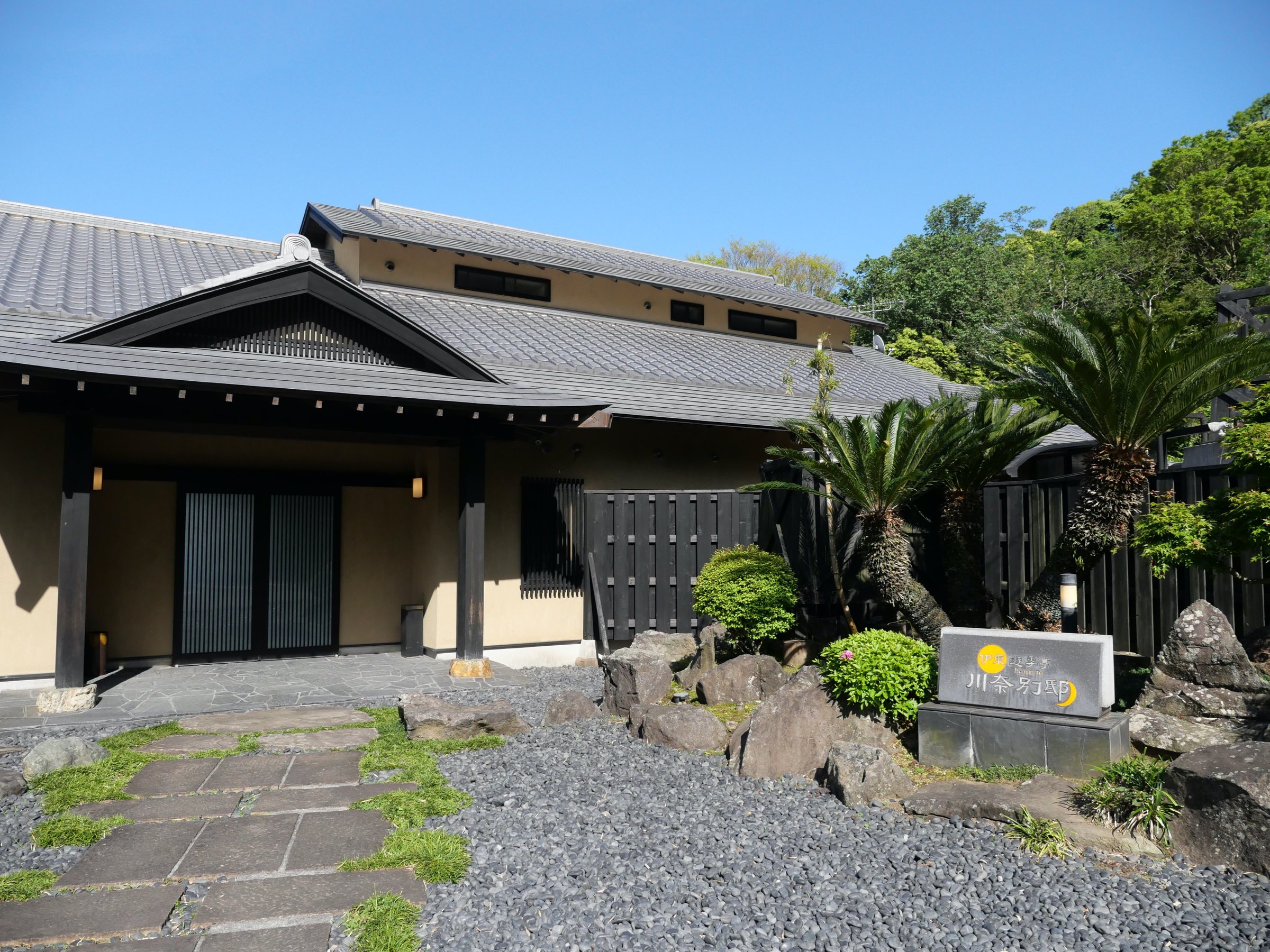 Arrival: low tiled roofs, palms and volcanic stone under a clear Izu sky.