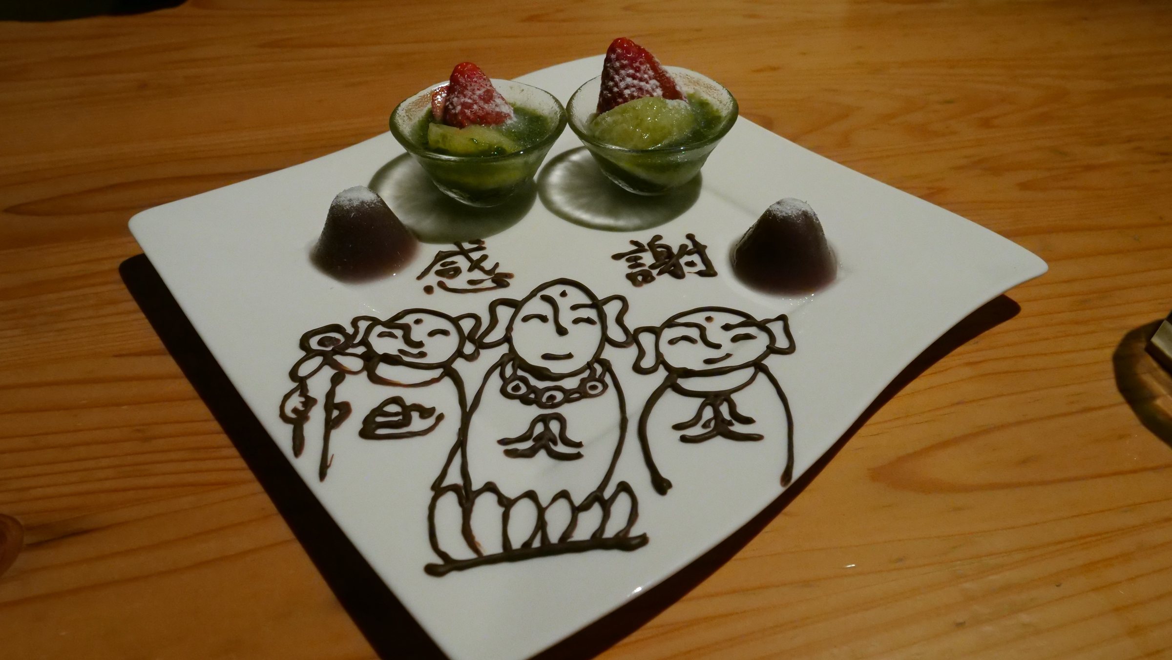 Dessert on a plate decorated in chocolate with smiling figures and the words "thank you".