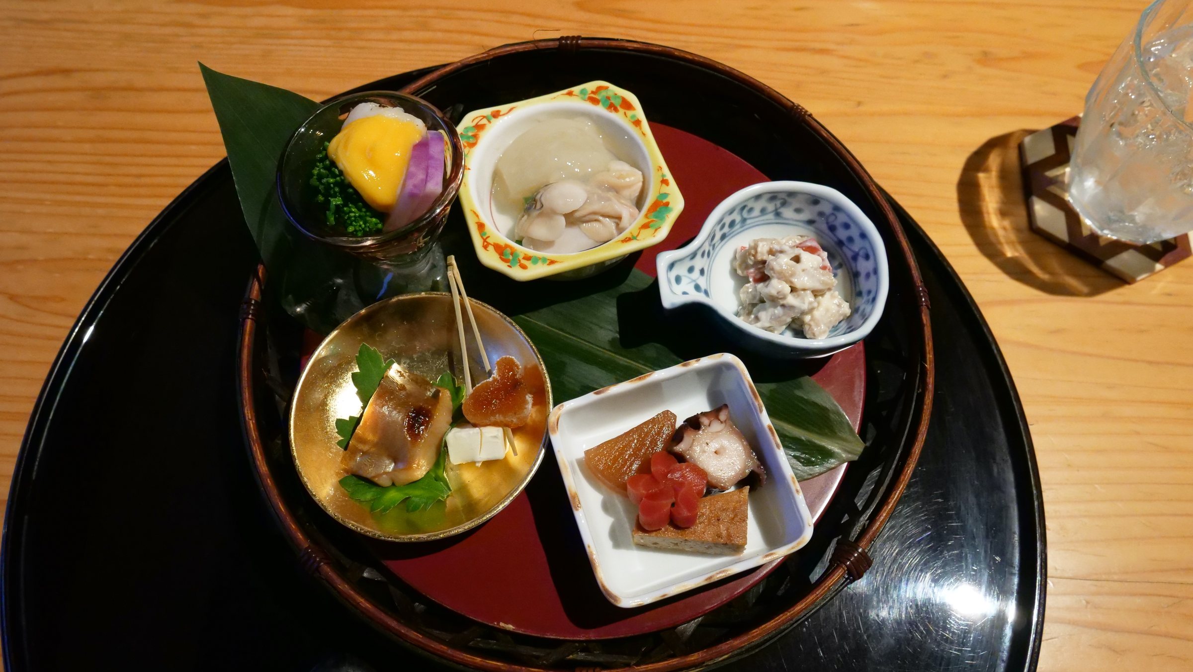 Seasonal appetisers in a cluster of small dishes on a round lacquer tray.
