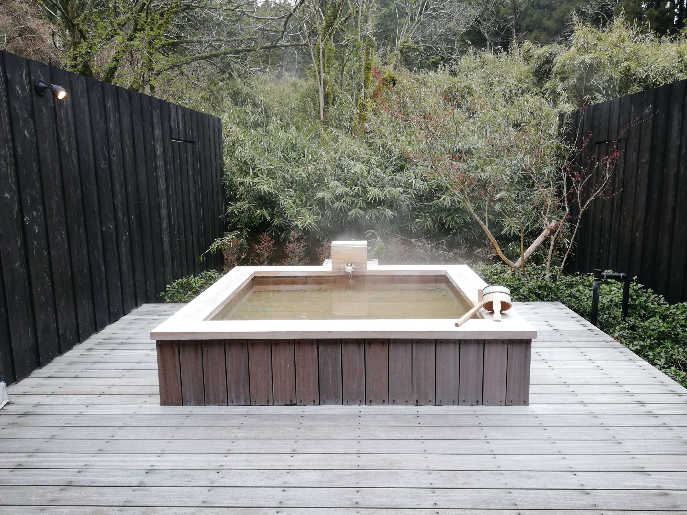 A private open-air bath by day, steam rising against the hillside.
