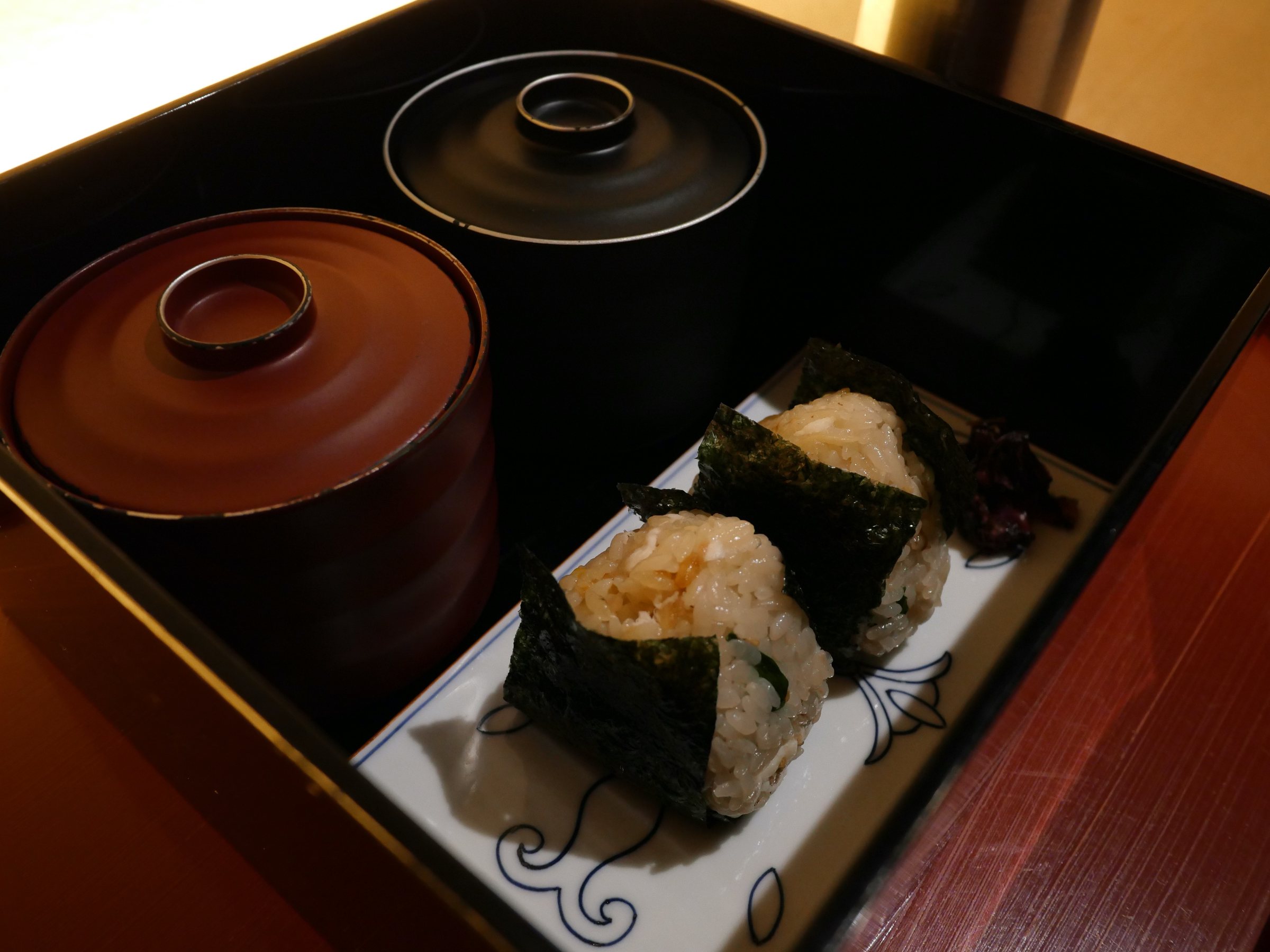 Inside: rice balls wrapped in nori, beside lidded bowls.