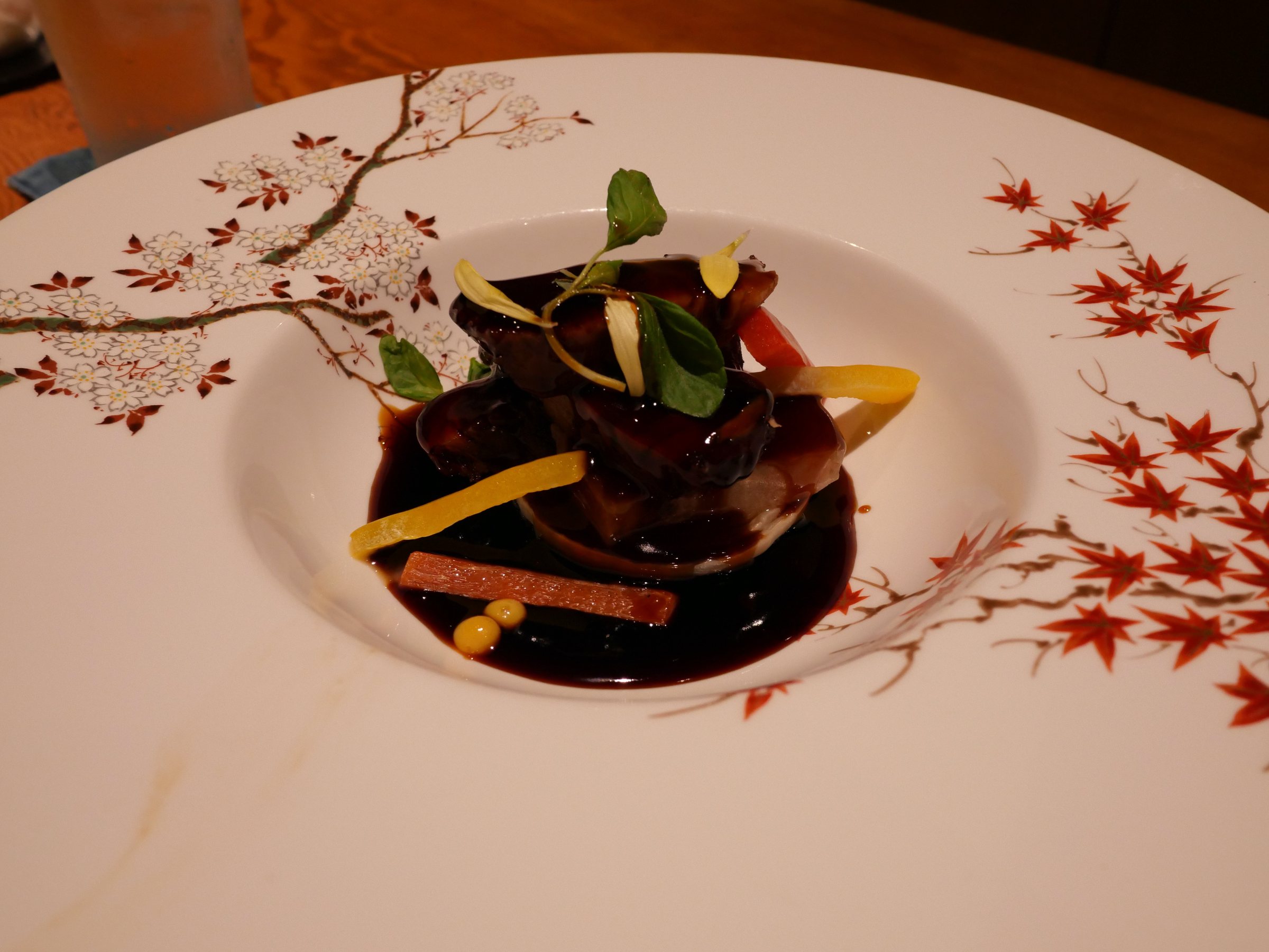 Pork in a dark, glossy sauce on a plate painted with red maples.