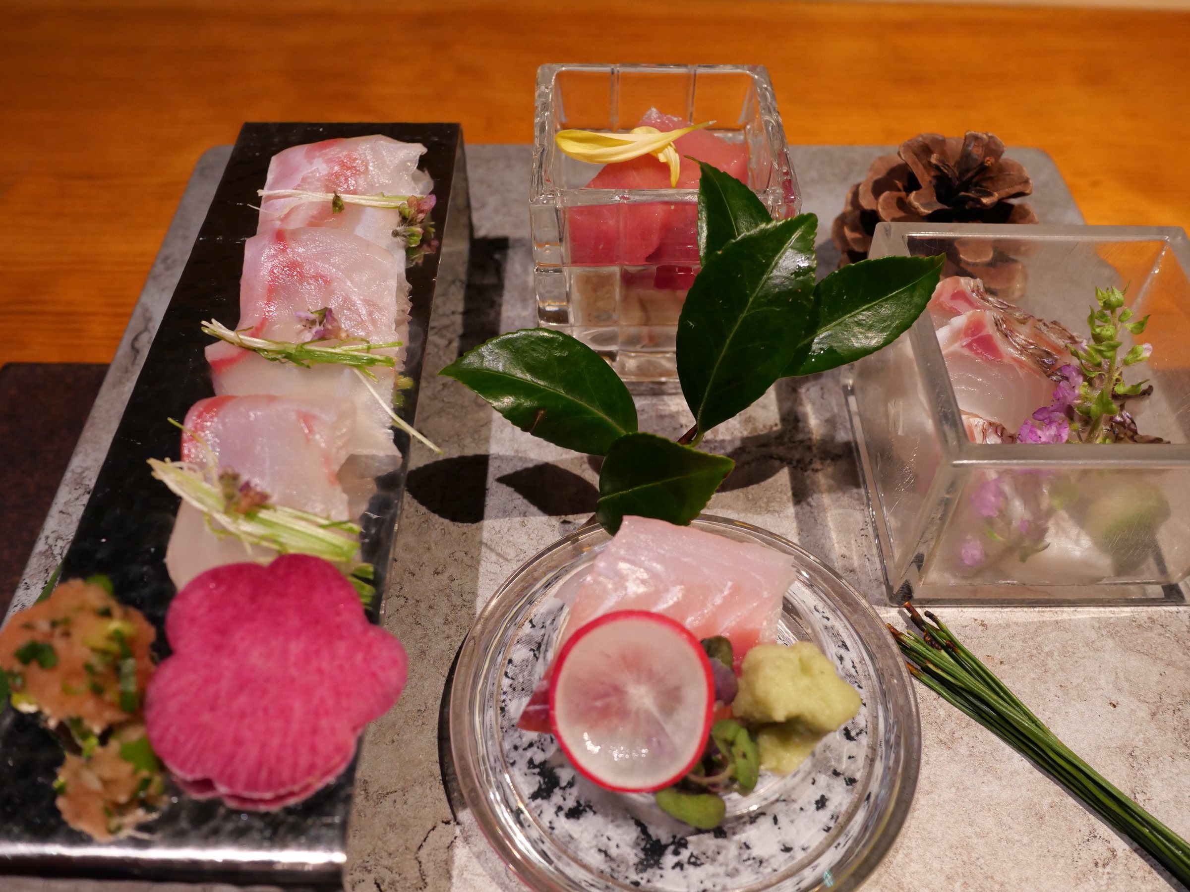Sashimi on stone and in glass, with radish, a pine cone and camellia leaves.