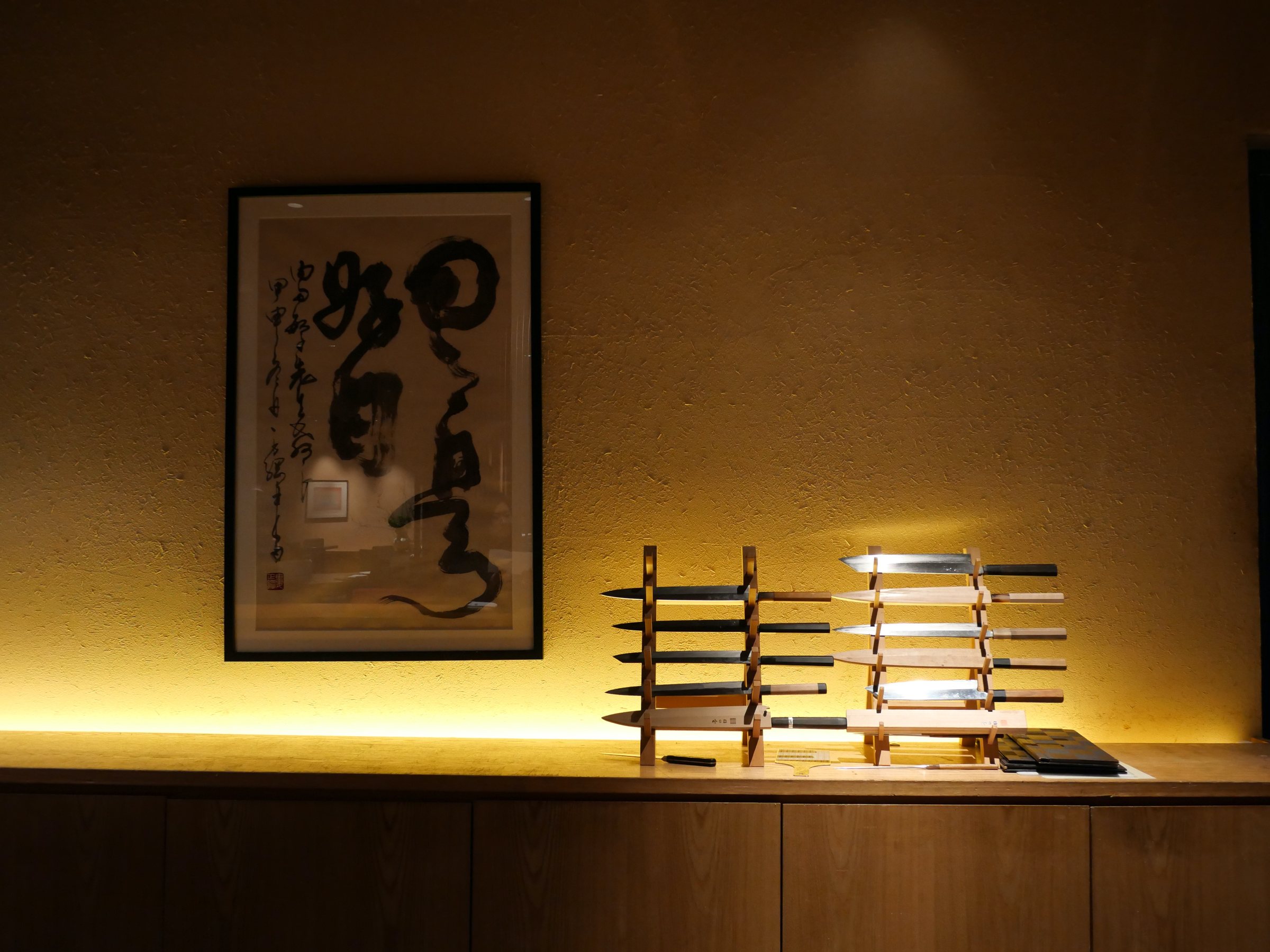 Behind the counter: bold calligraphy and a row of kitchen knives on display.