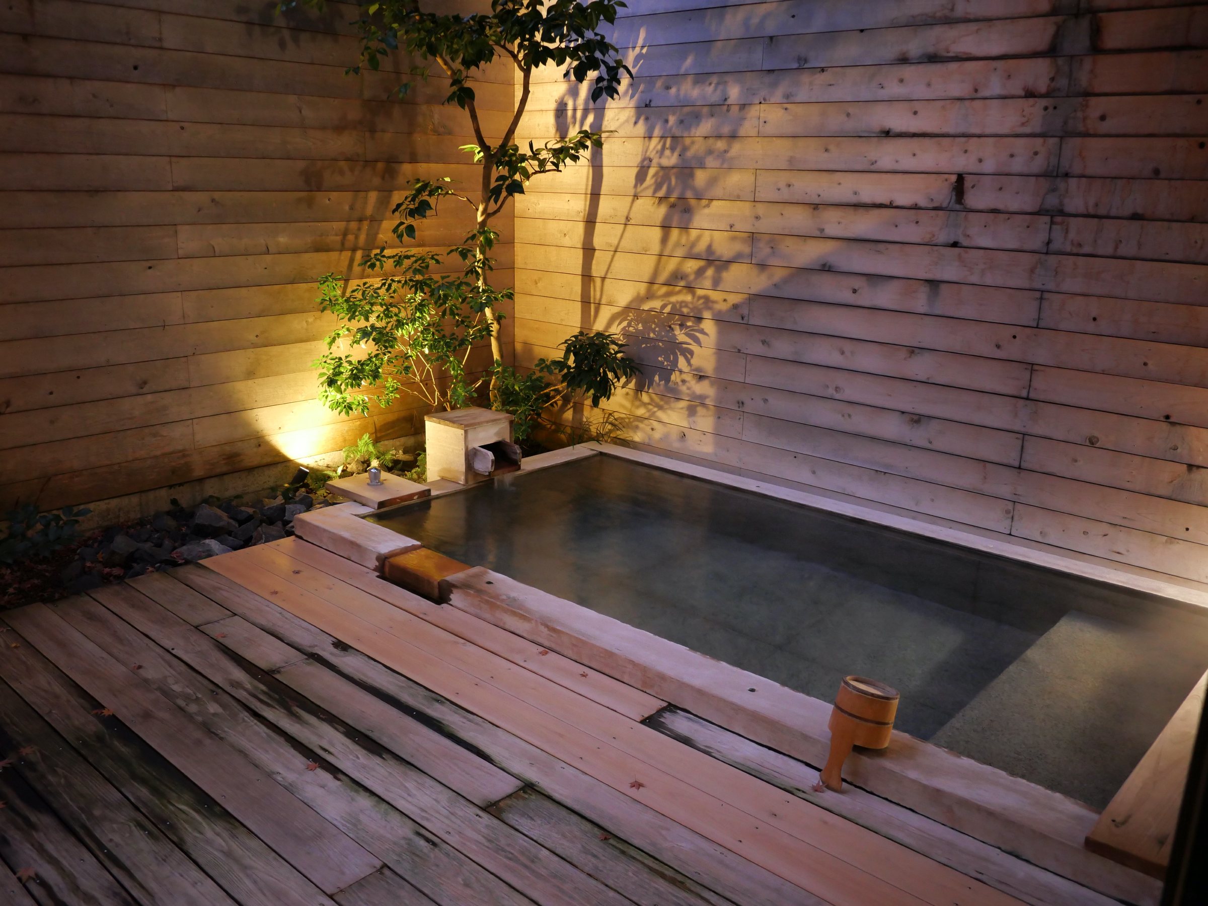 The room's open-air bath, softly lit against weathered timber.
