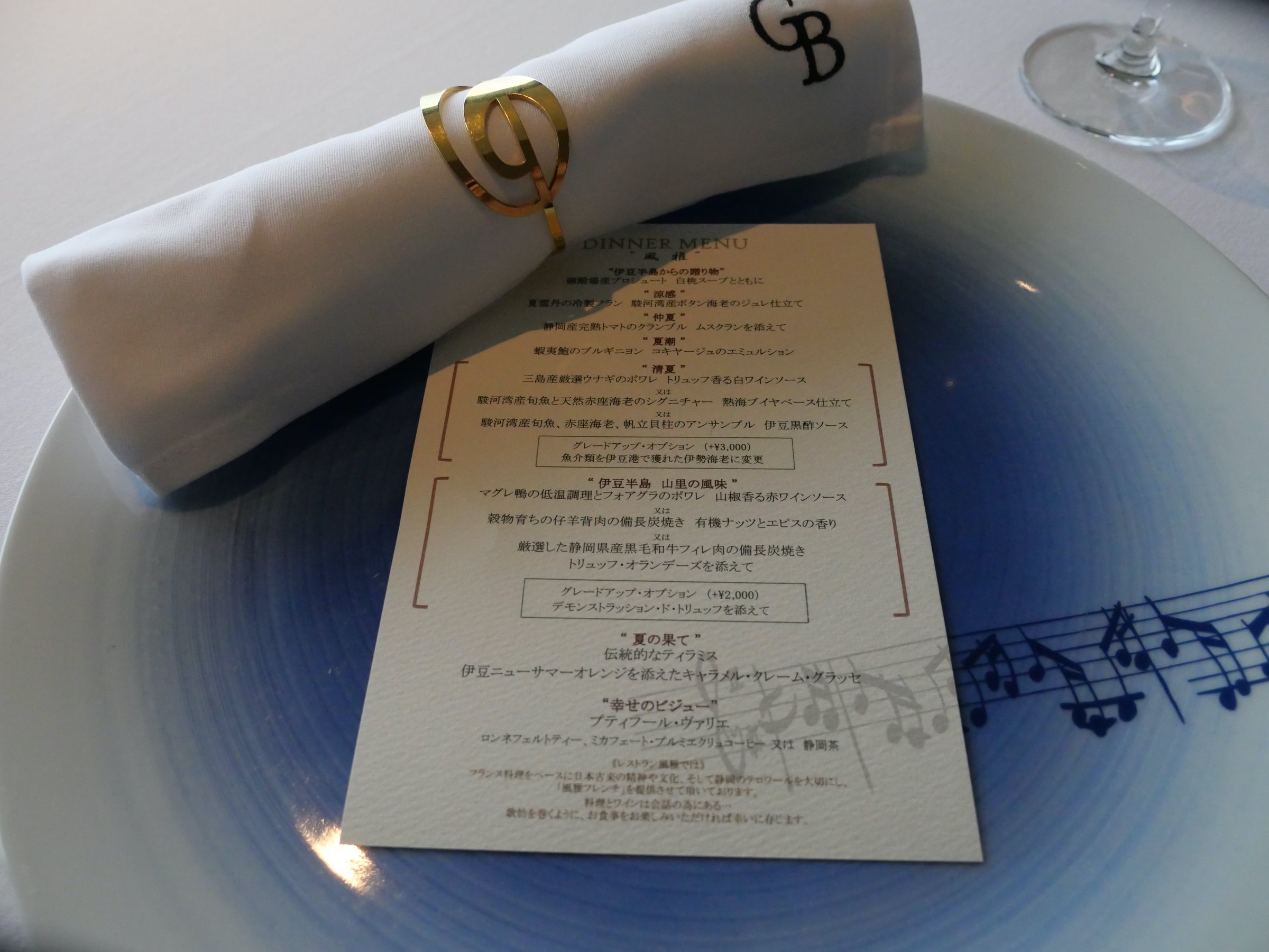 The menu, laid on the plate beside a monogrammed napkin.