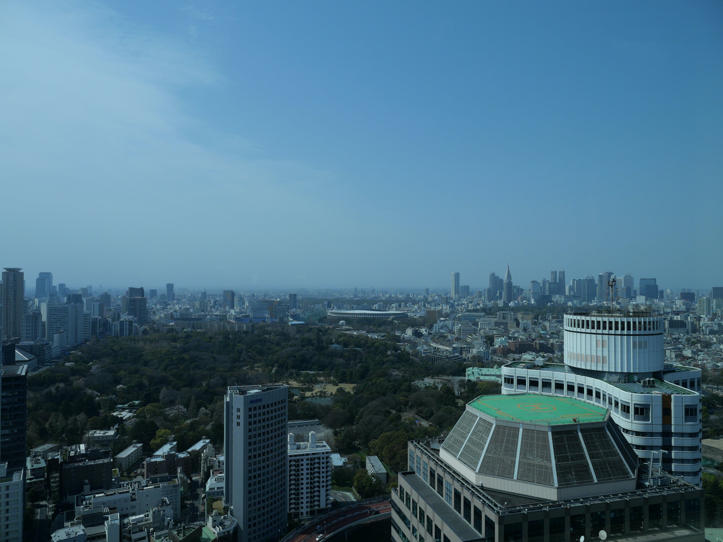 Looking west across green parkland toward Shinjuku, the rooftop of a neighboring hotel in the foreground.