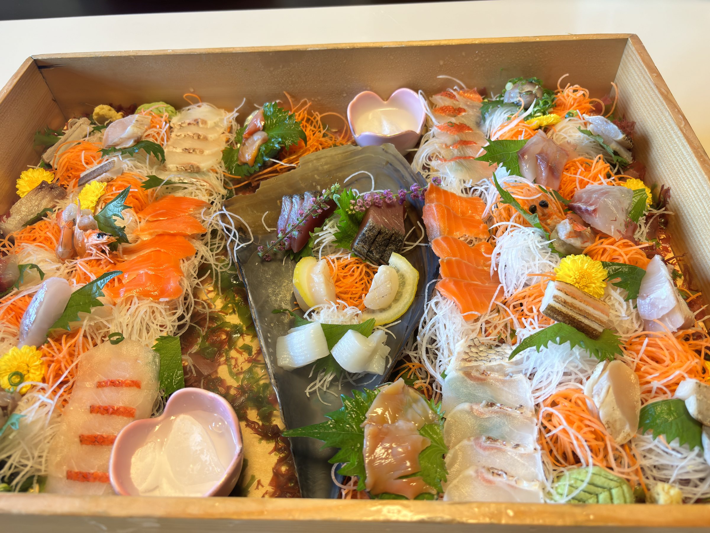 The wooden box of sashimi, garnished with flowers and shredded vegetables.