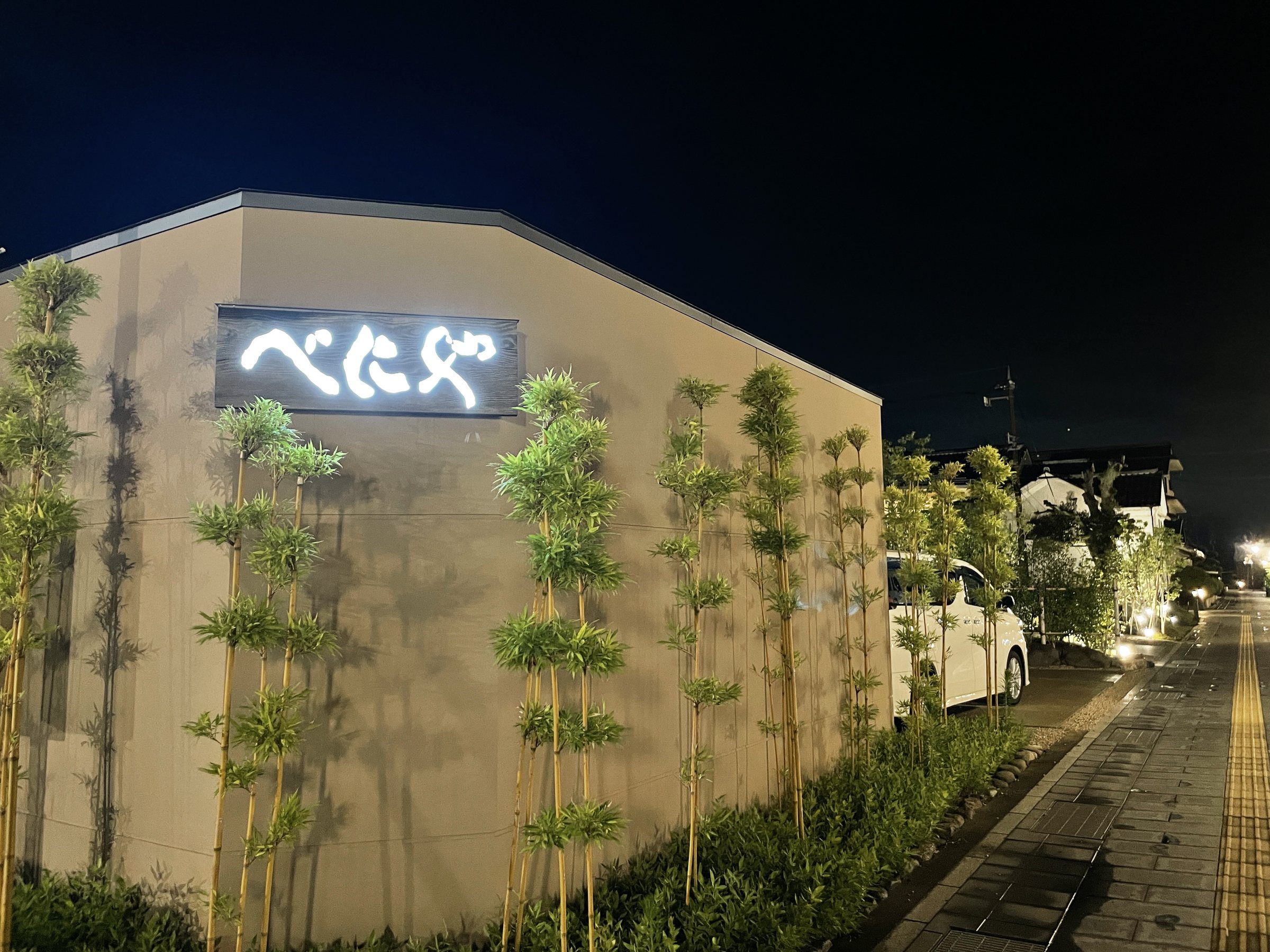 The new building at night, its sign lit above a row of slender bamboo.