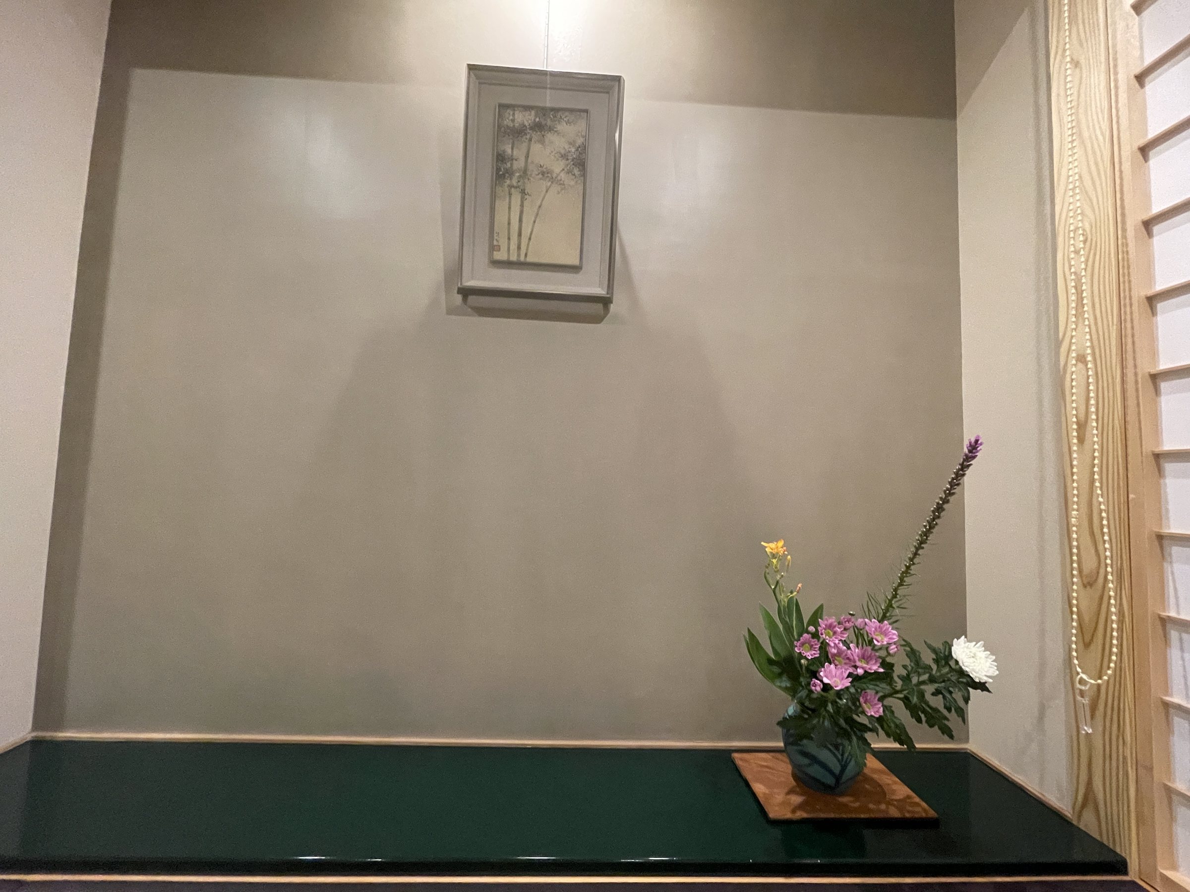 The tokonoma, with an arrangement of fresh flowers on a deep green base and a hanging picture.