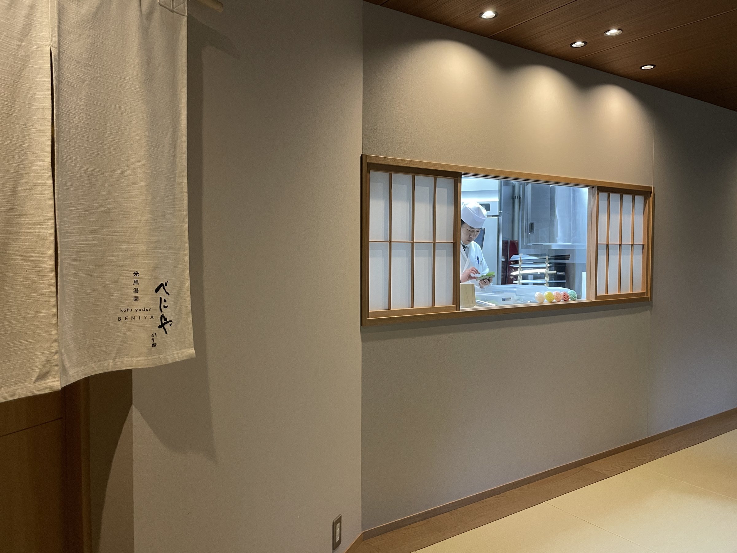 The corridor with its noren curtain and the kitchen window set into the wall.