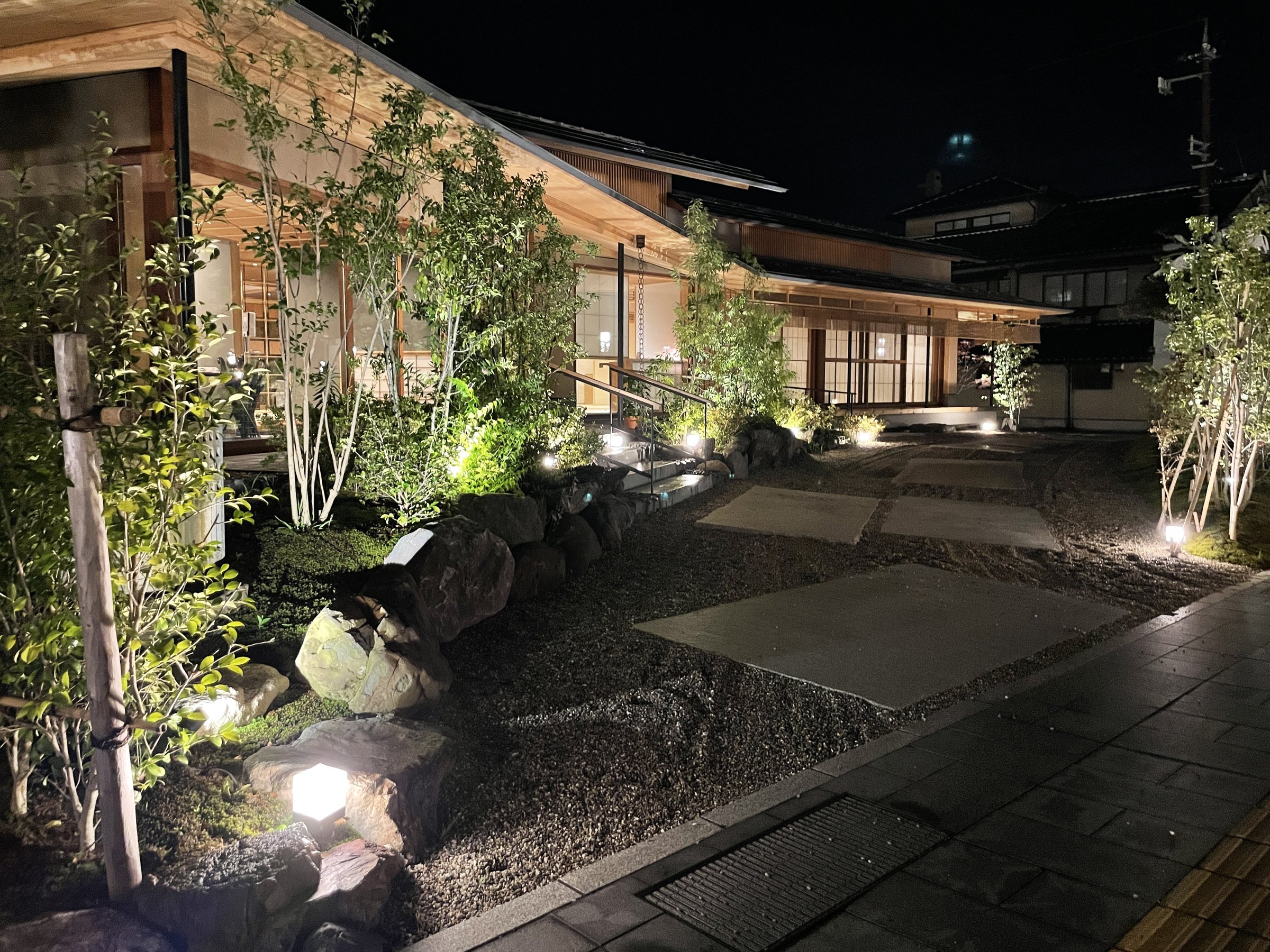 The garden at night, with its stone paving and lit trees.