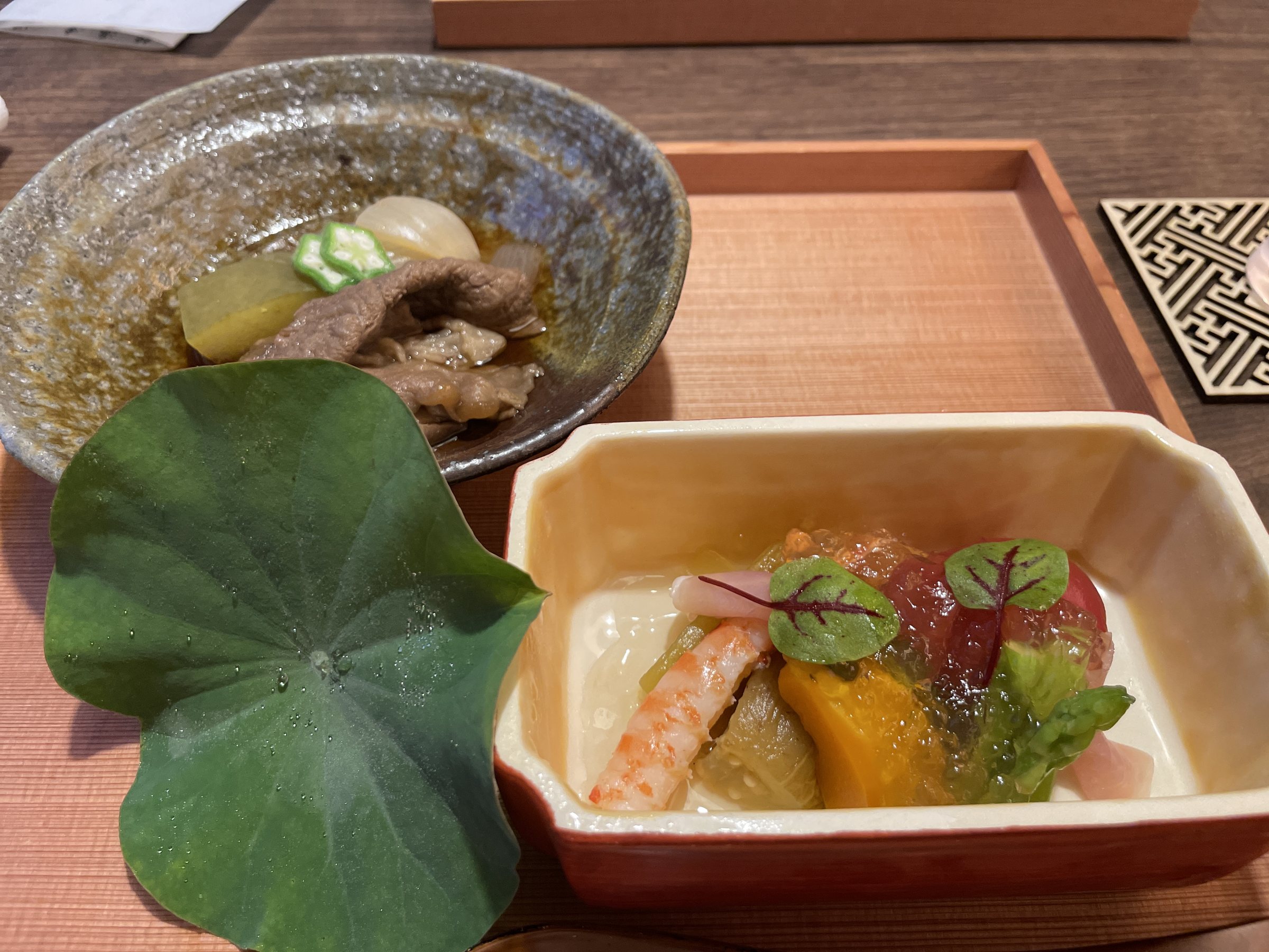 Beef simmered in a small bowl, and vegetables with shrimp in a square dish.