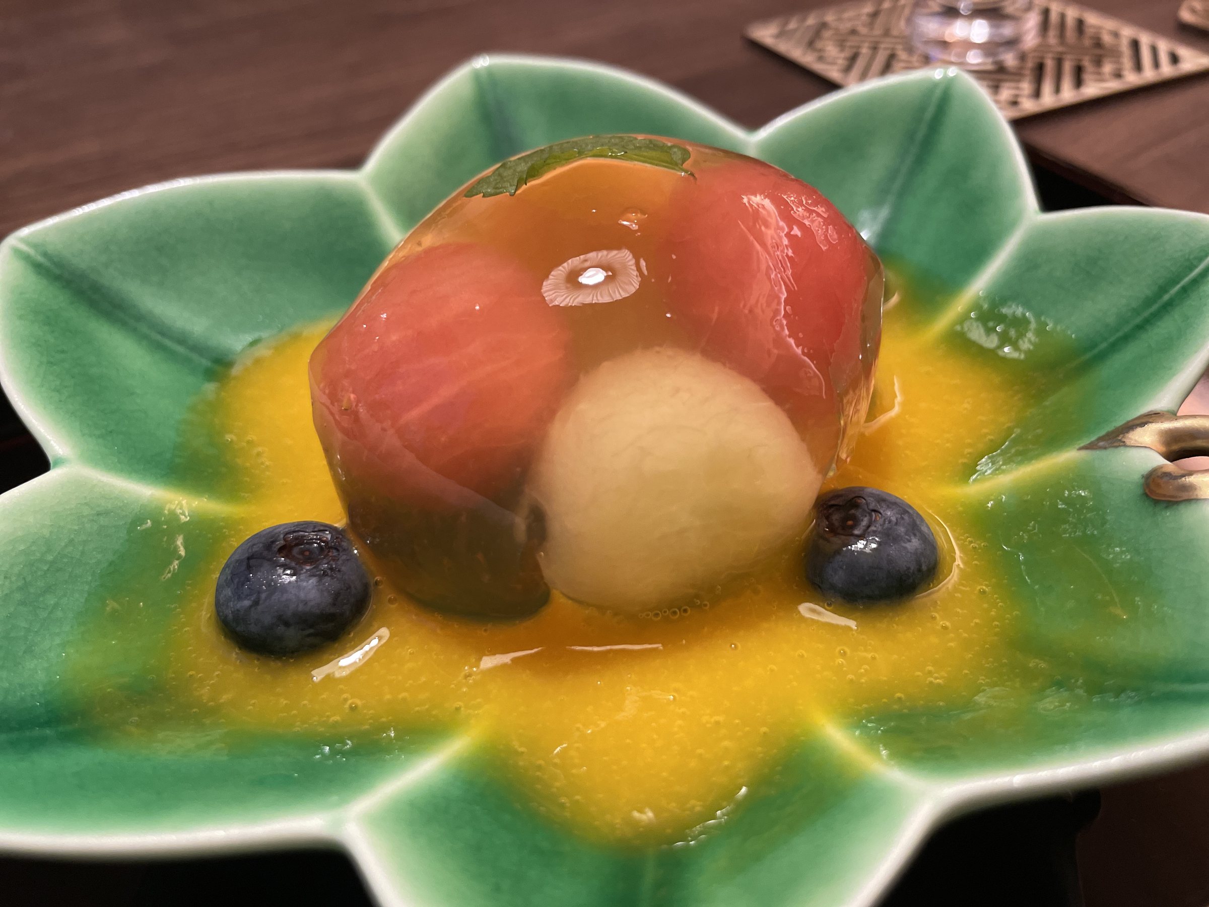 A fruit jelly terrine with blueberries, in a yellow sauce on a green dish.