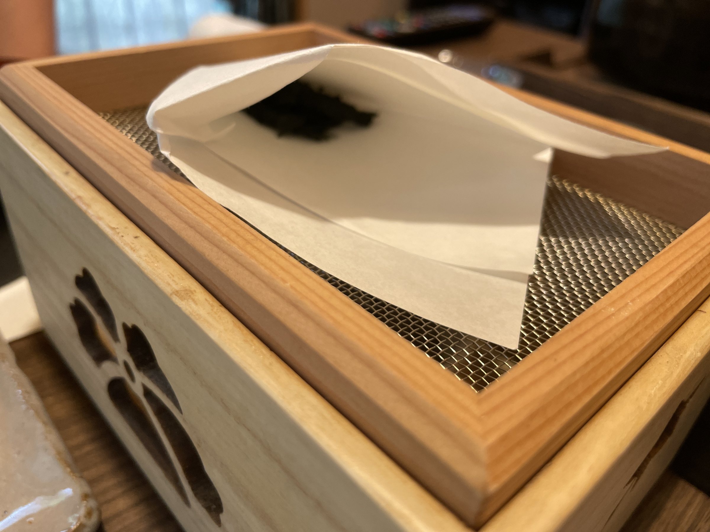 Dried wakame being toasted on a mesh in a wooden box.