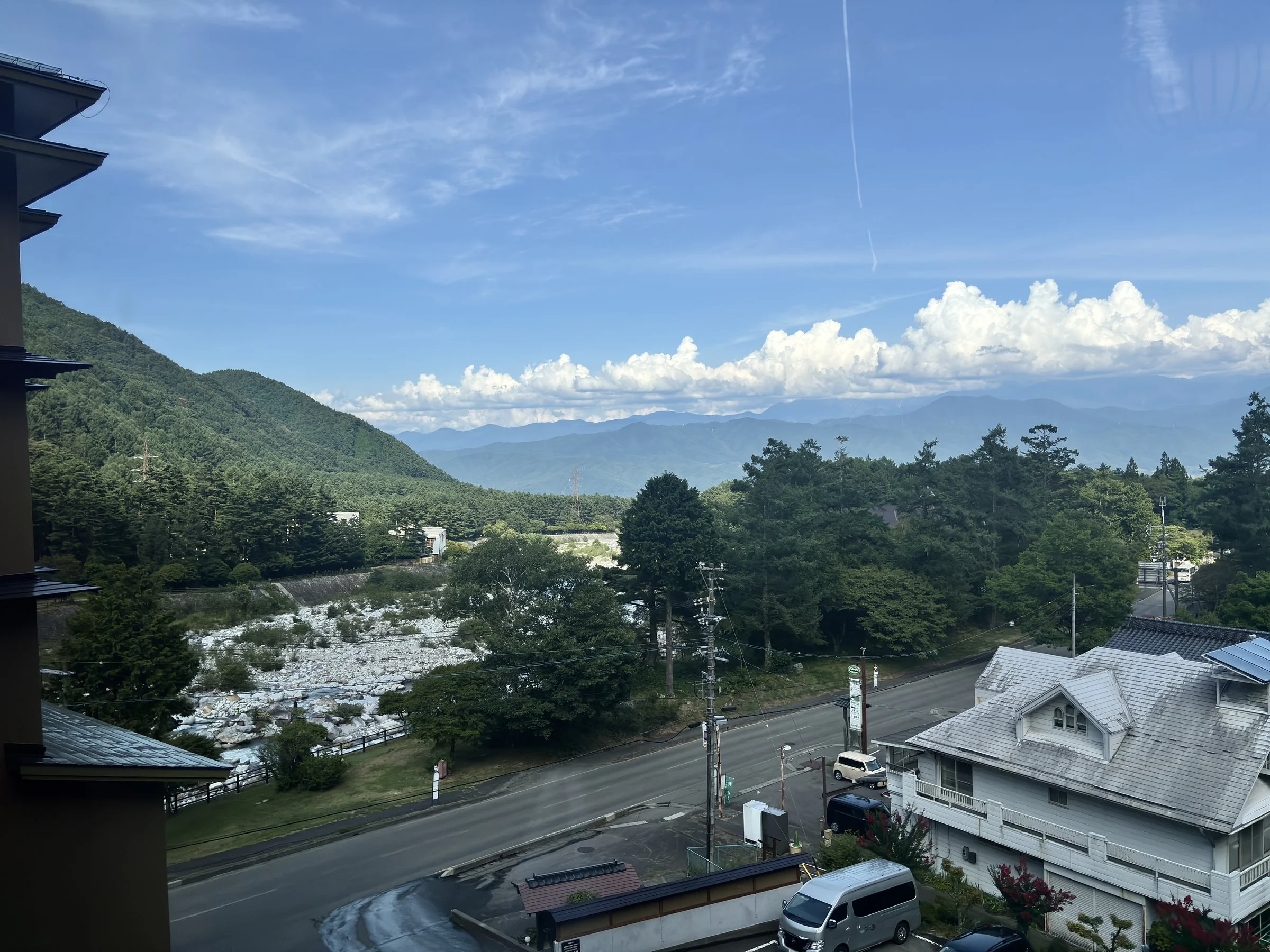 The view from the ryokan over the Komagane highlands: forested slopes, a wide riverbed and mountains under summer cloud.