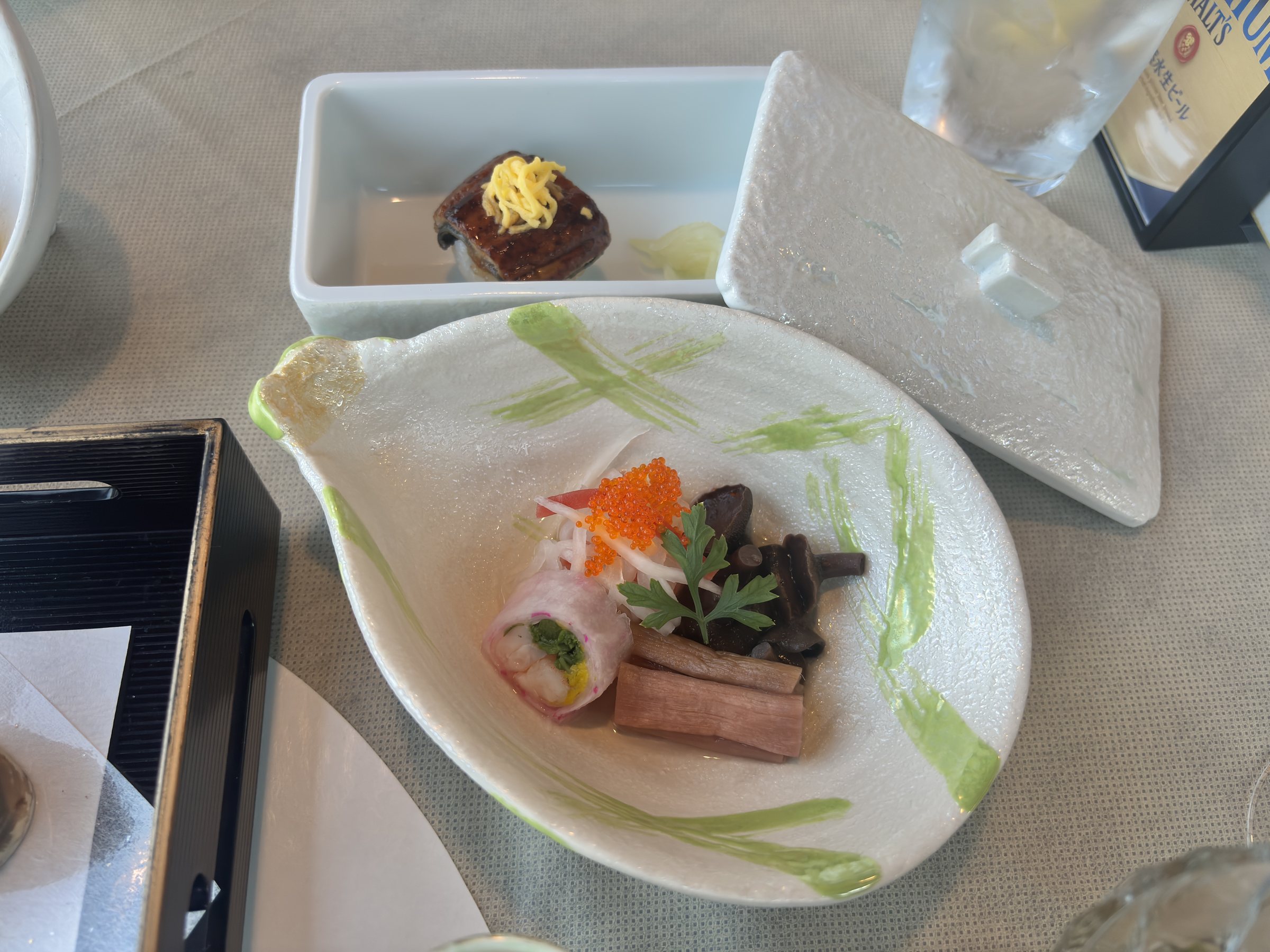 A leaf-shaped plate of rolled appetisers with greens and a small orange garnish.