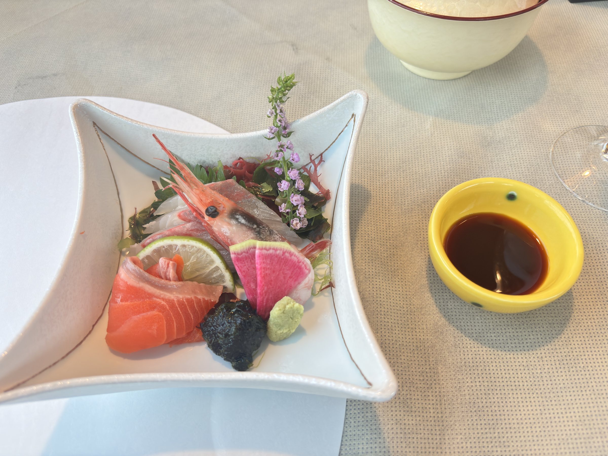 A sashimi platter of salmon, prawn and other fish, with soy sauce on the side.