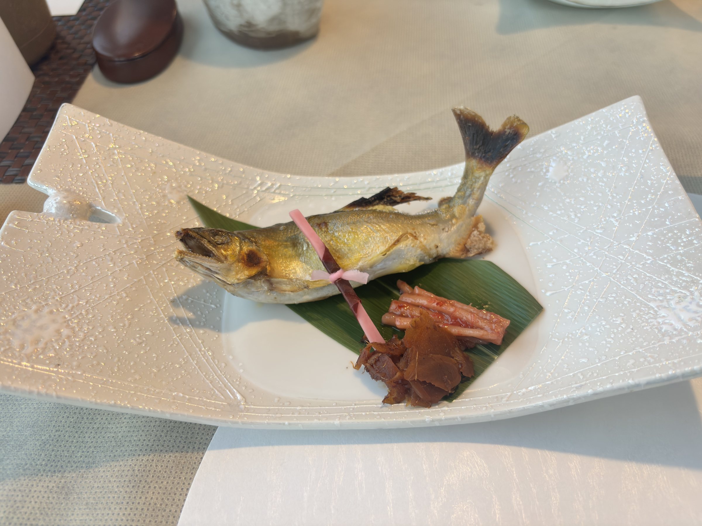 A whole grilled sweetfish on a long white plate.