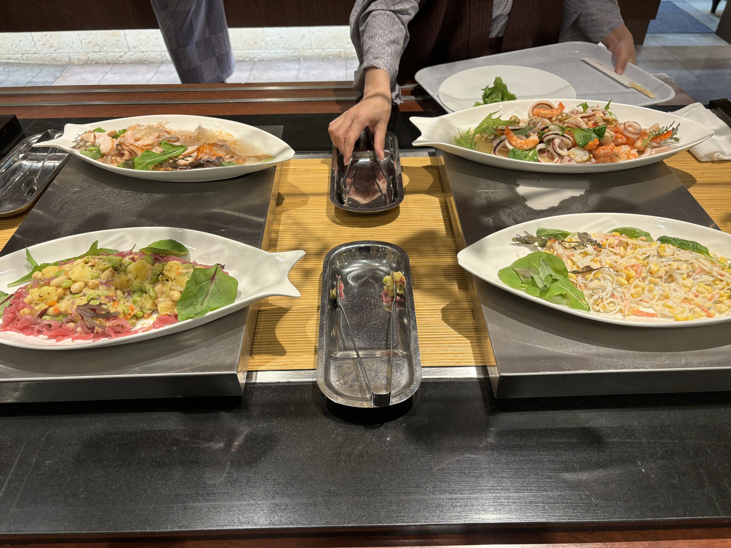 Salads and noodle dishes on long plates.