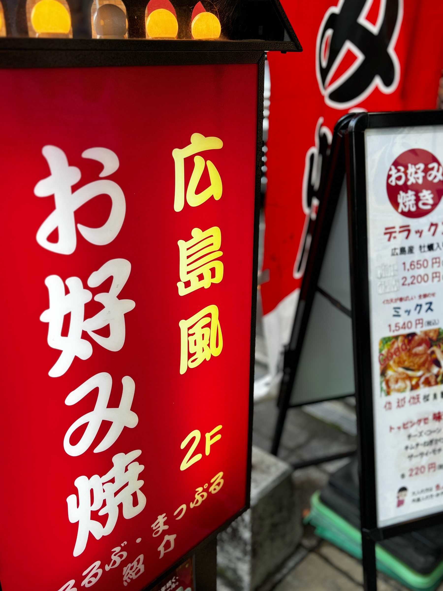 A red okonomiyaki sign outside a second-floor restaurant.