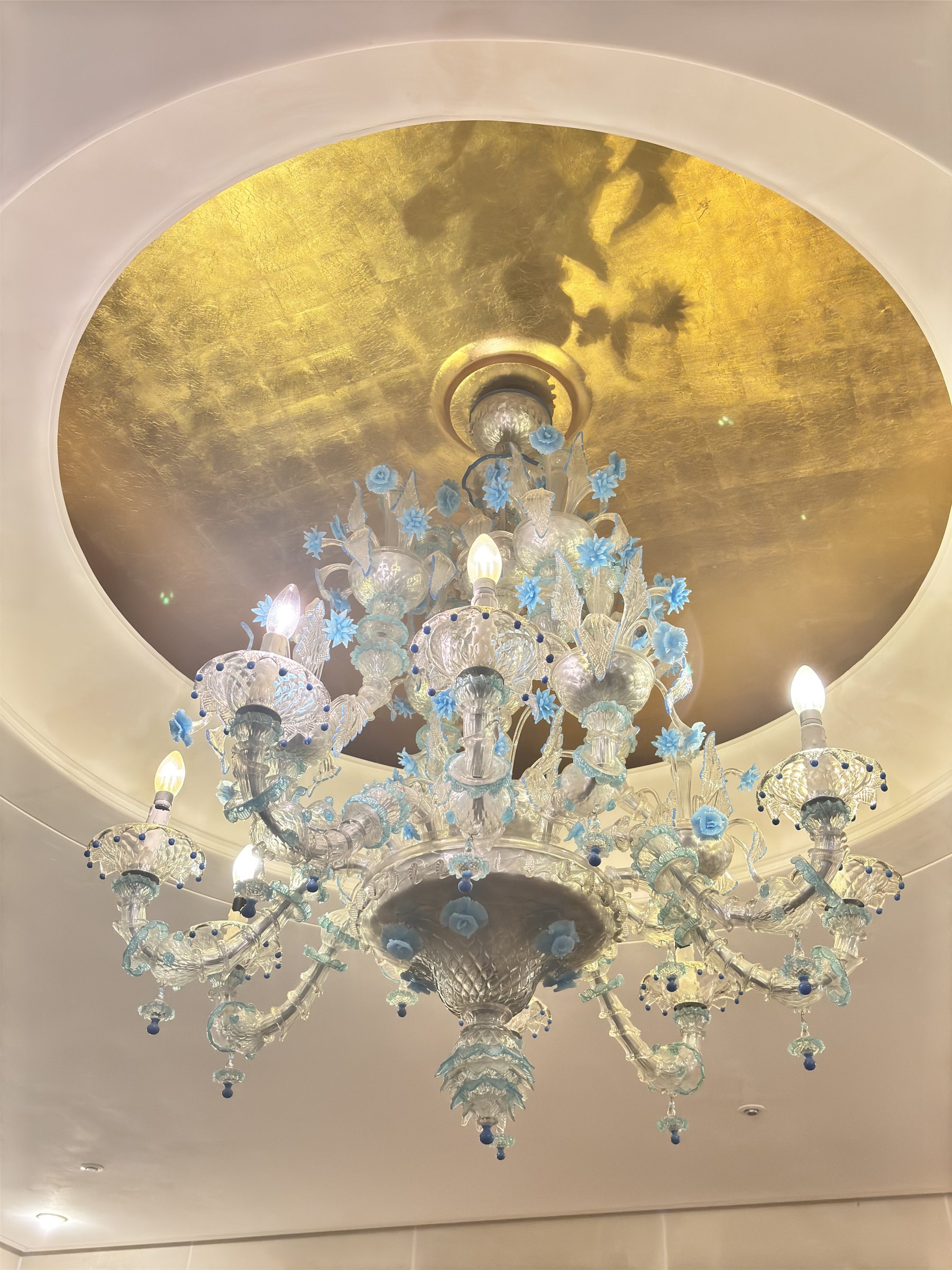 A chandelier of blue and clear glass beneath a gold-leaf dome.