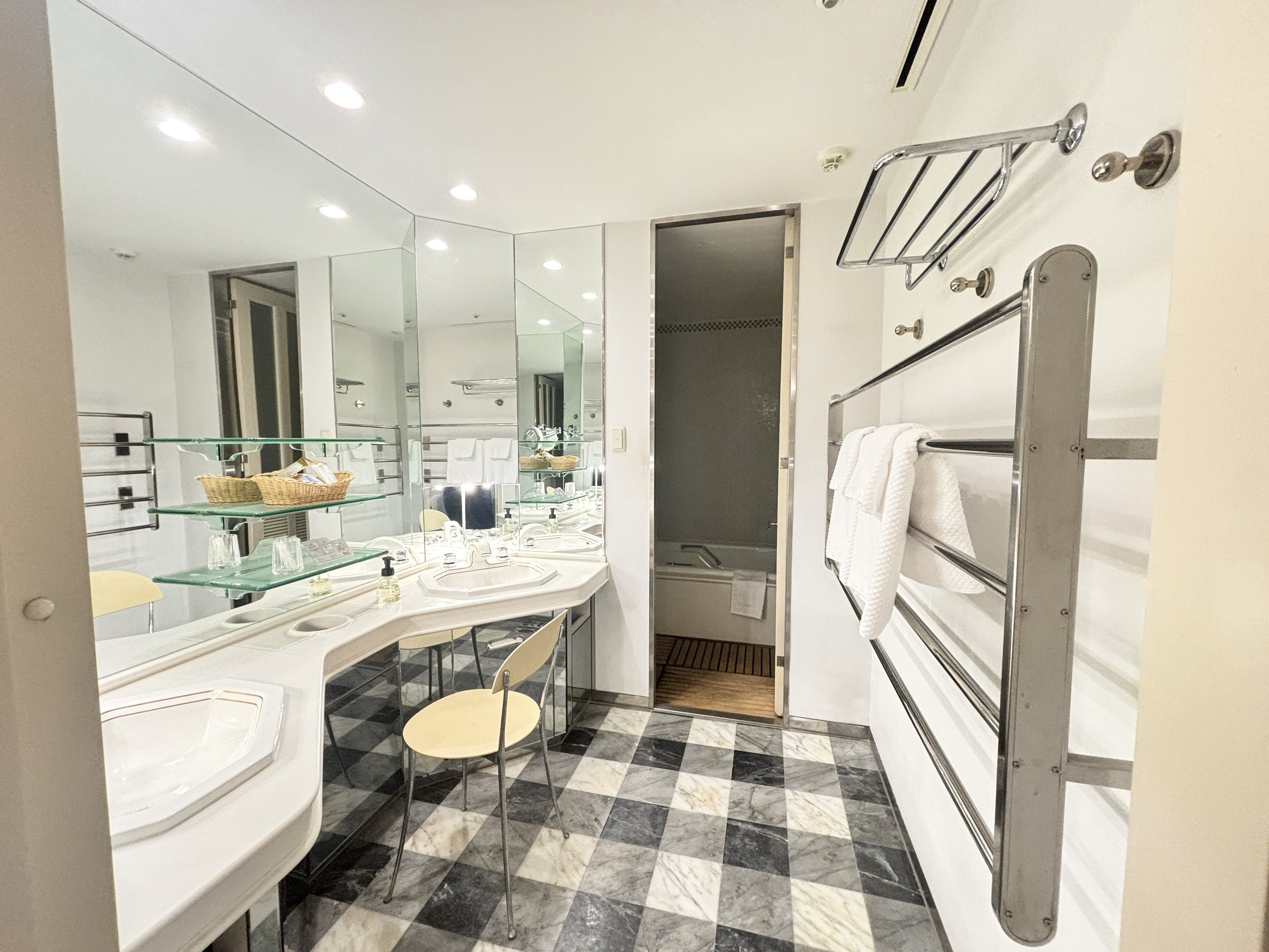 The bathroom, with a long white vanity, glass shelves and a chequered marble floor.