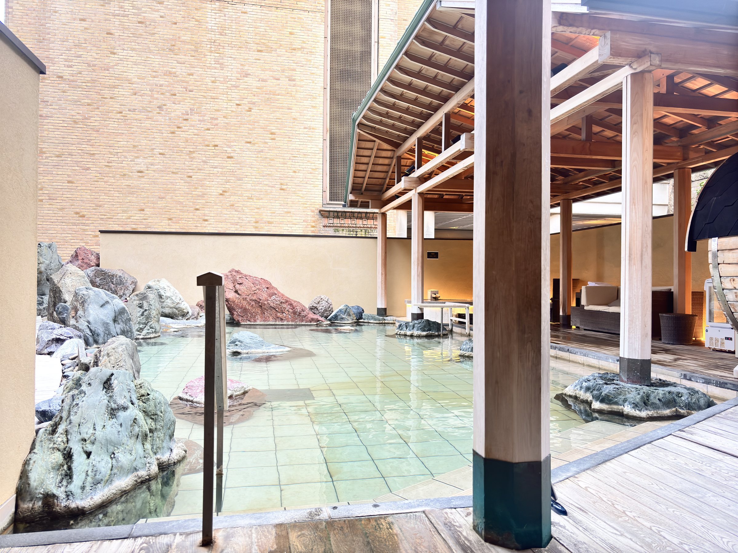 The open-air bath, edged with rocks, beside a wooden pavilion.