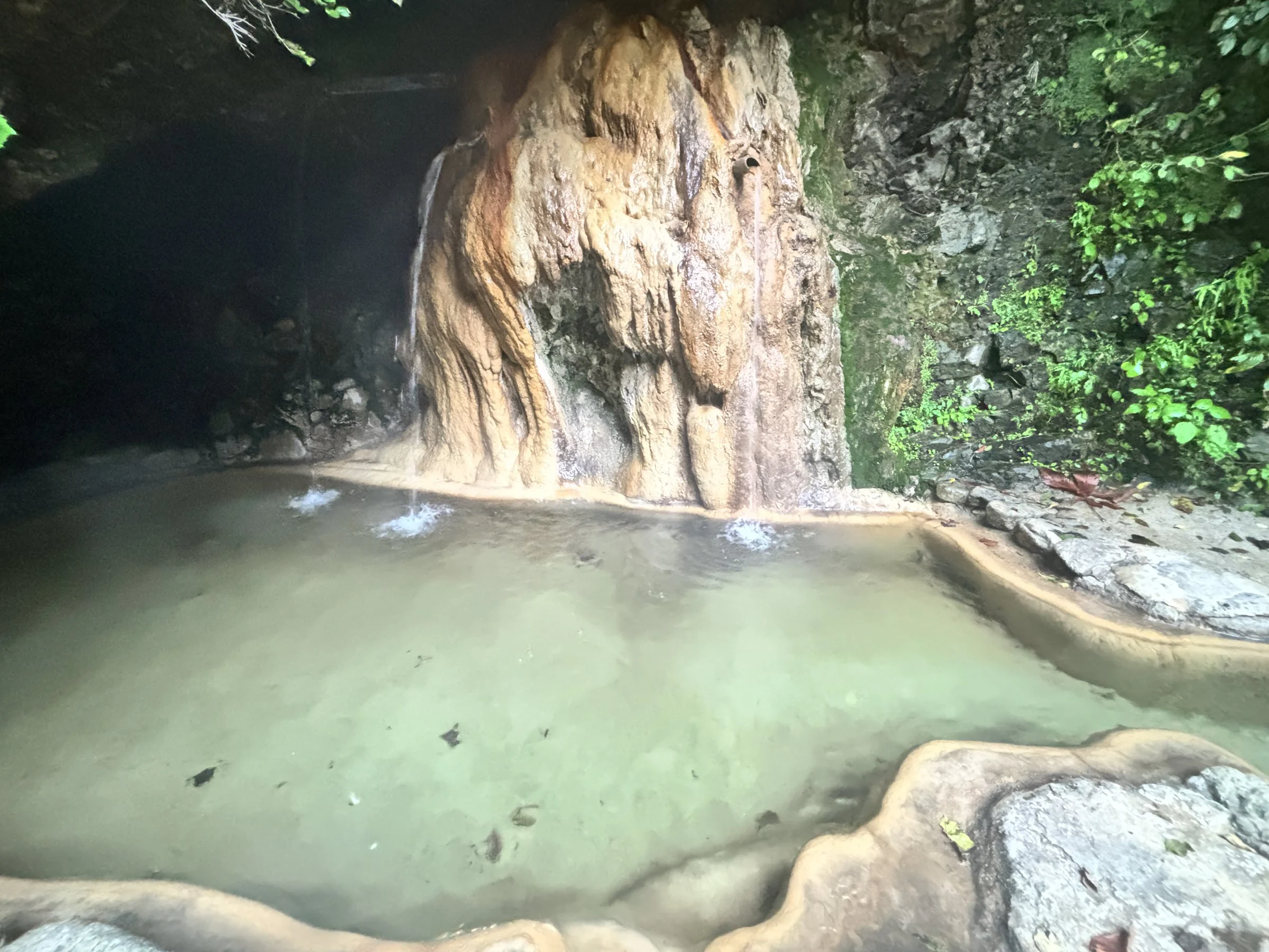 Hot water spilling over orange mineral deposits into the cave pool.