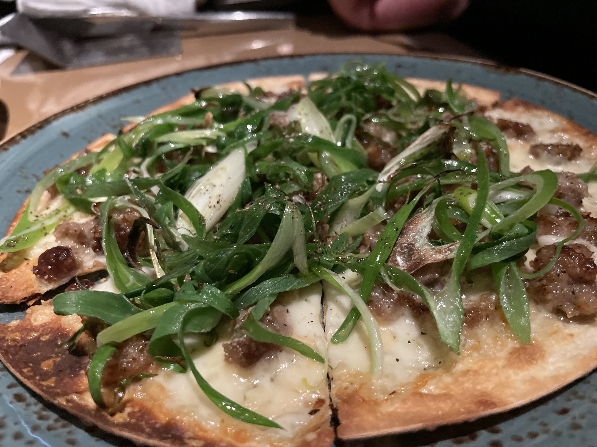 Pizza topped with a tangle of green Kujo leek over Iberico pork.