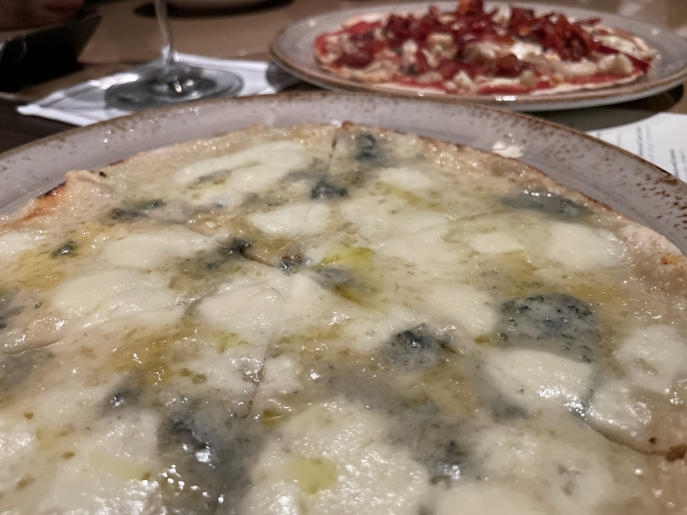 A Gorgonzola pizza with pools of blue cheese, another pizza behind it.