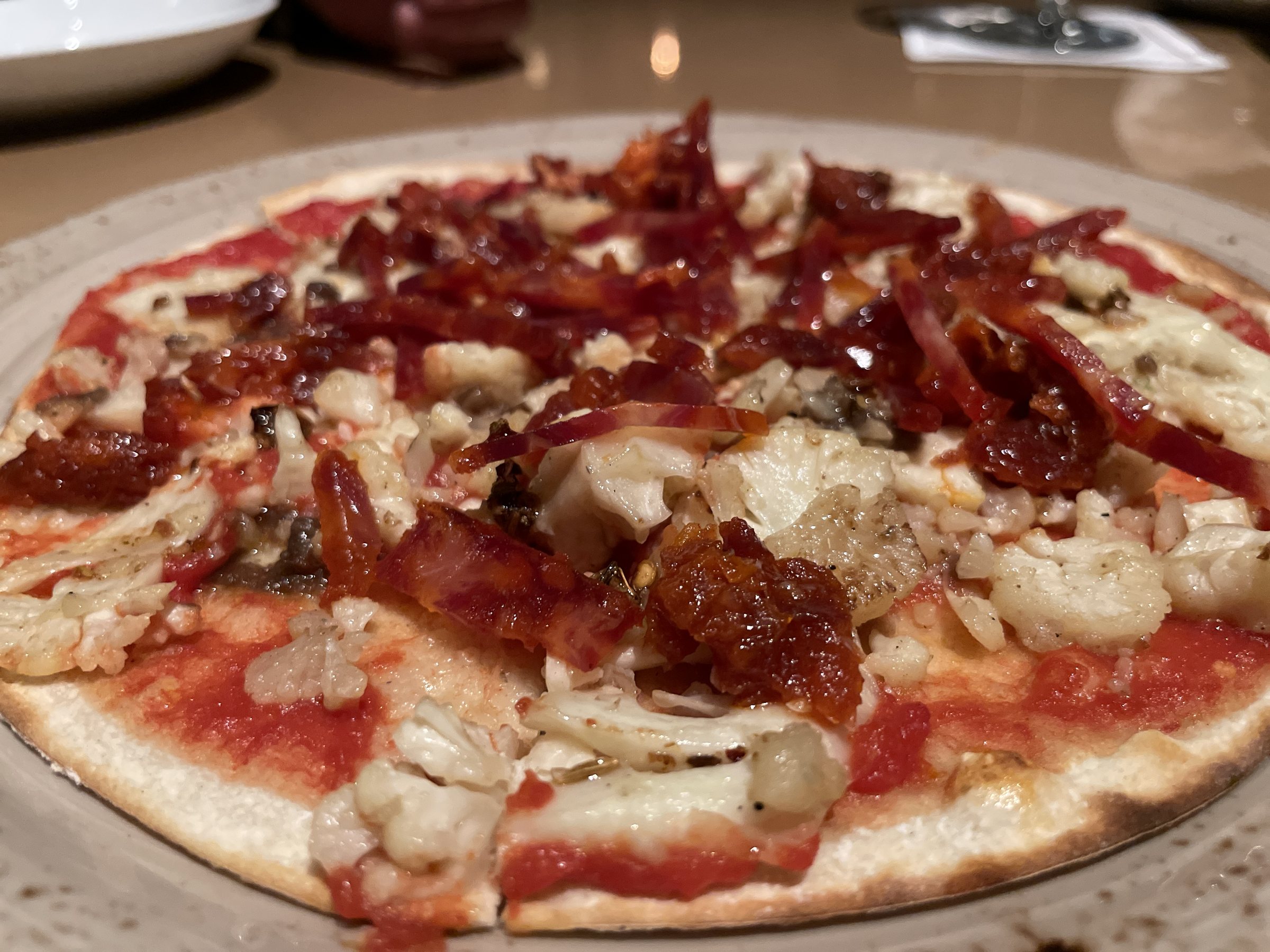 Pizza with a tomato base, slices of cured meat and pale florets.
