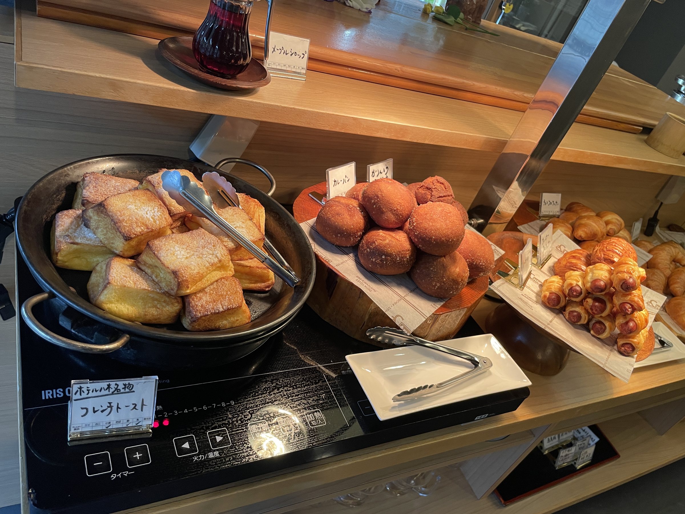 A pan of toast-like slices and a tray of sugared buns on the hot counter.