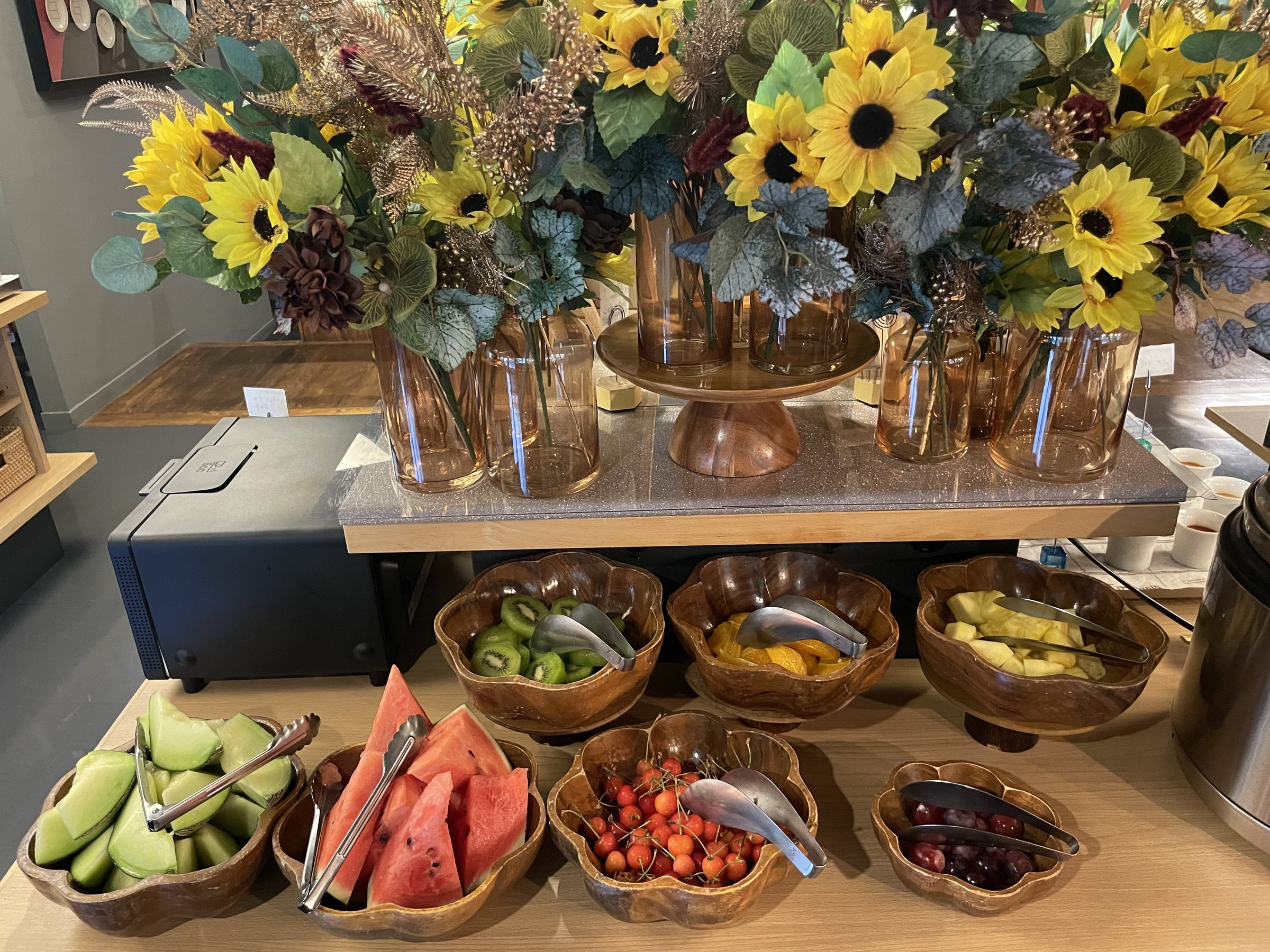 Bowls of fruit, including watermelon, beneath an arrangement of sunflowers.