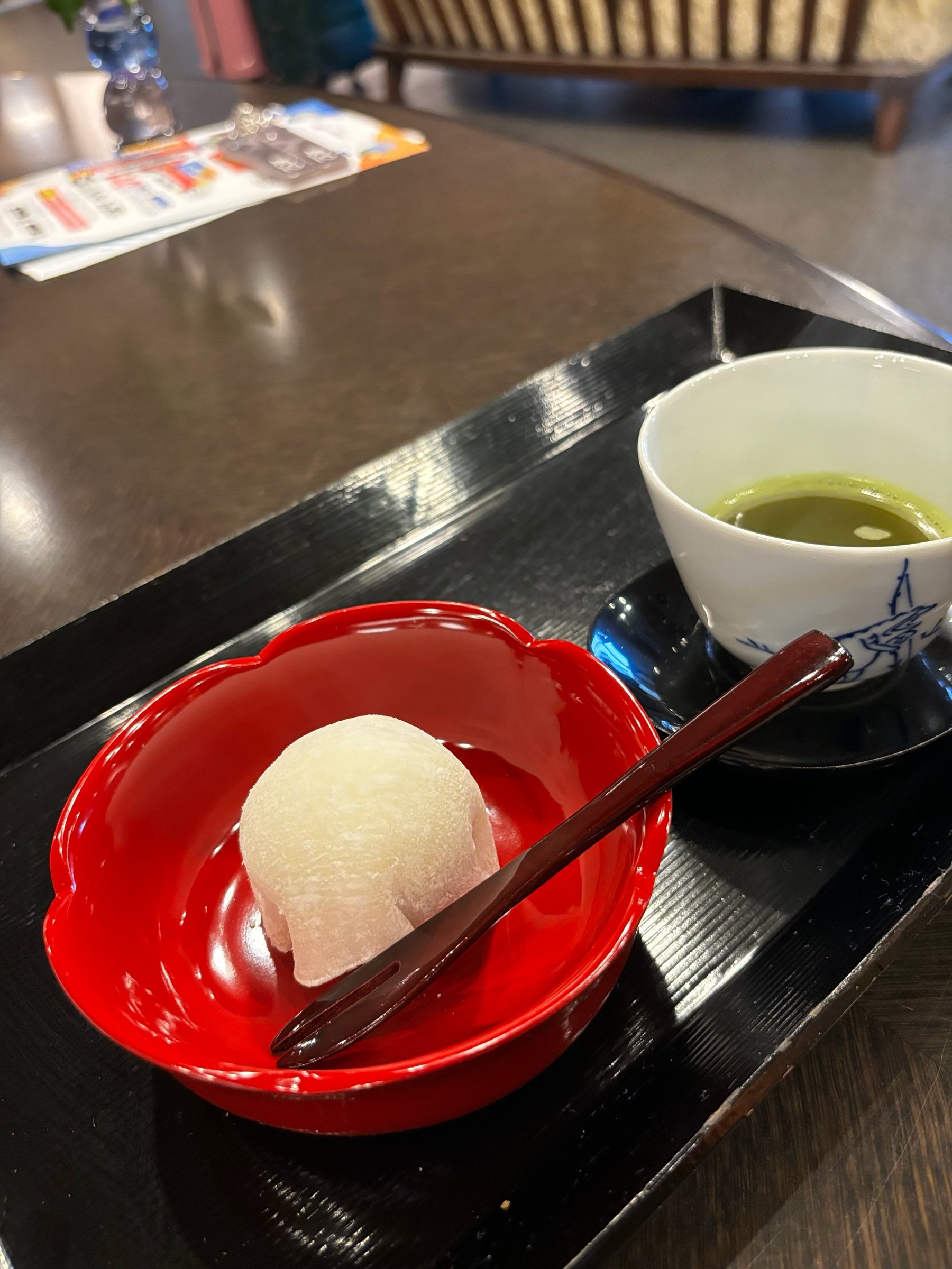 A white fruit daifuku in a red lacquer bowl, with a cup of green tea.