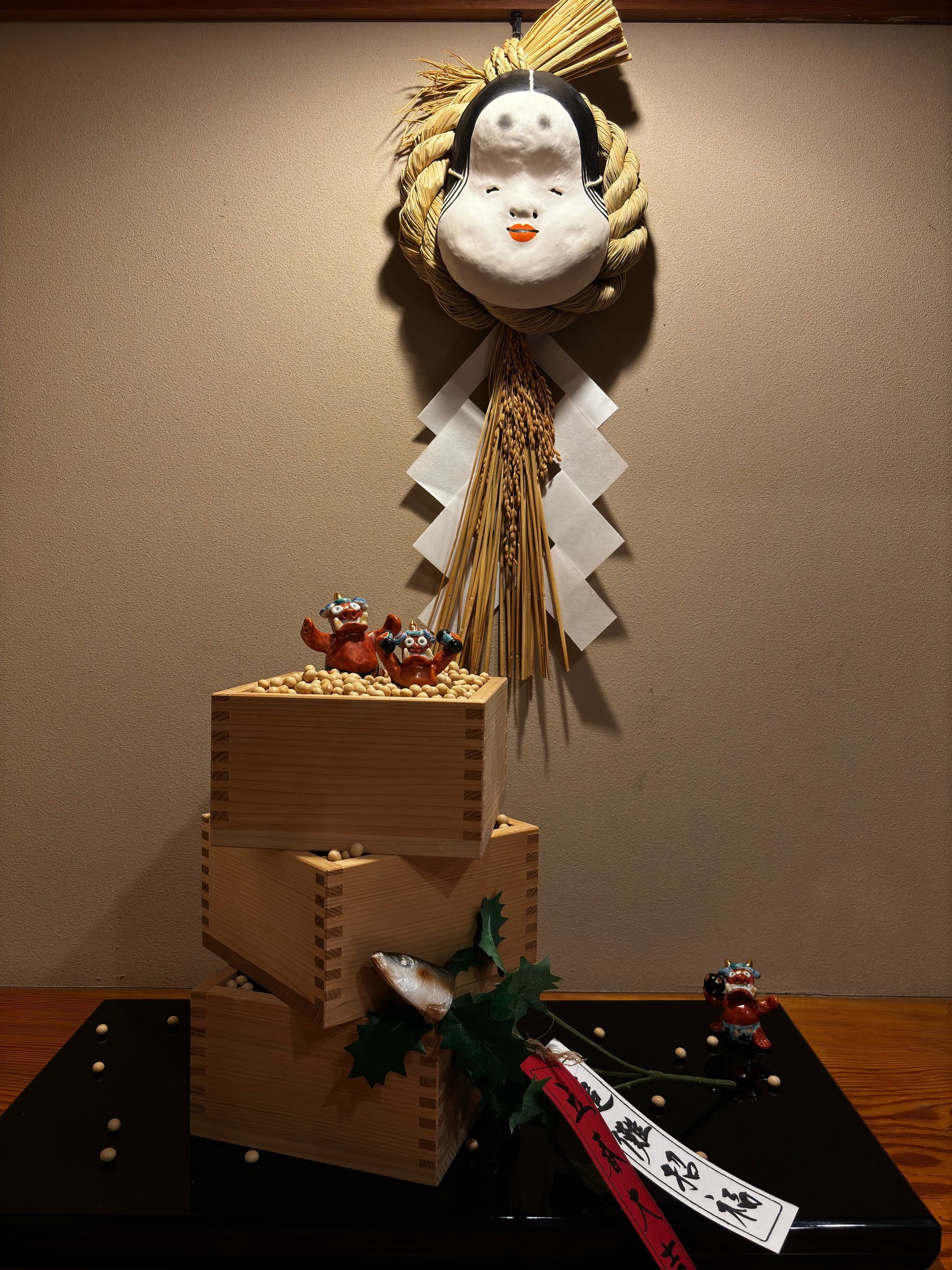 A seasonal New Year decoration: an Okame mask, straw rope, paper streamers and wooden measuring boxes.