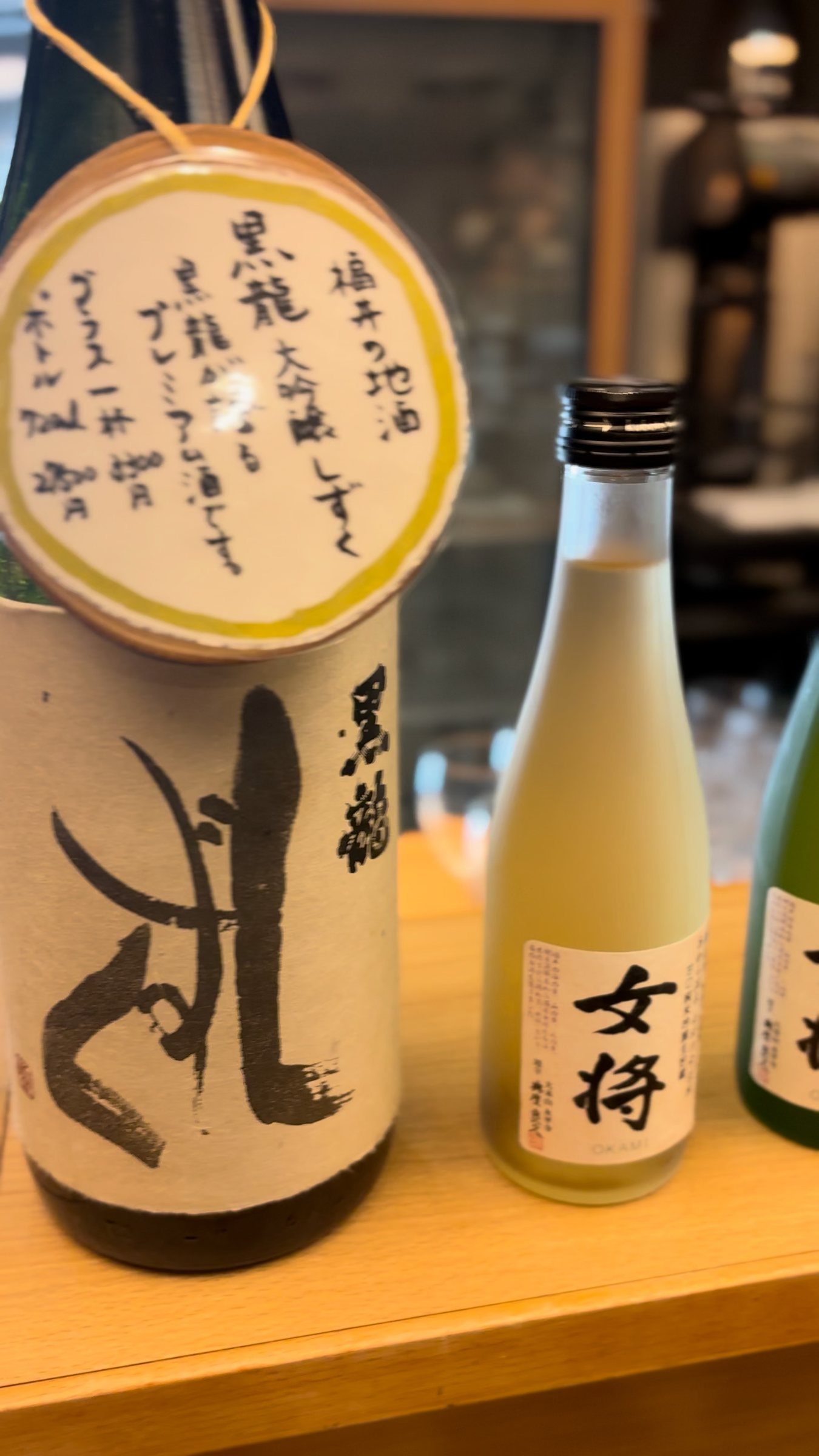 A bottle of Kokuryu sake with a handwritten tag, beside a small bottle labeled “Okami”.