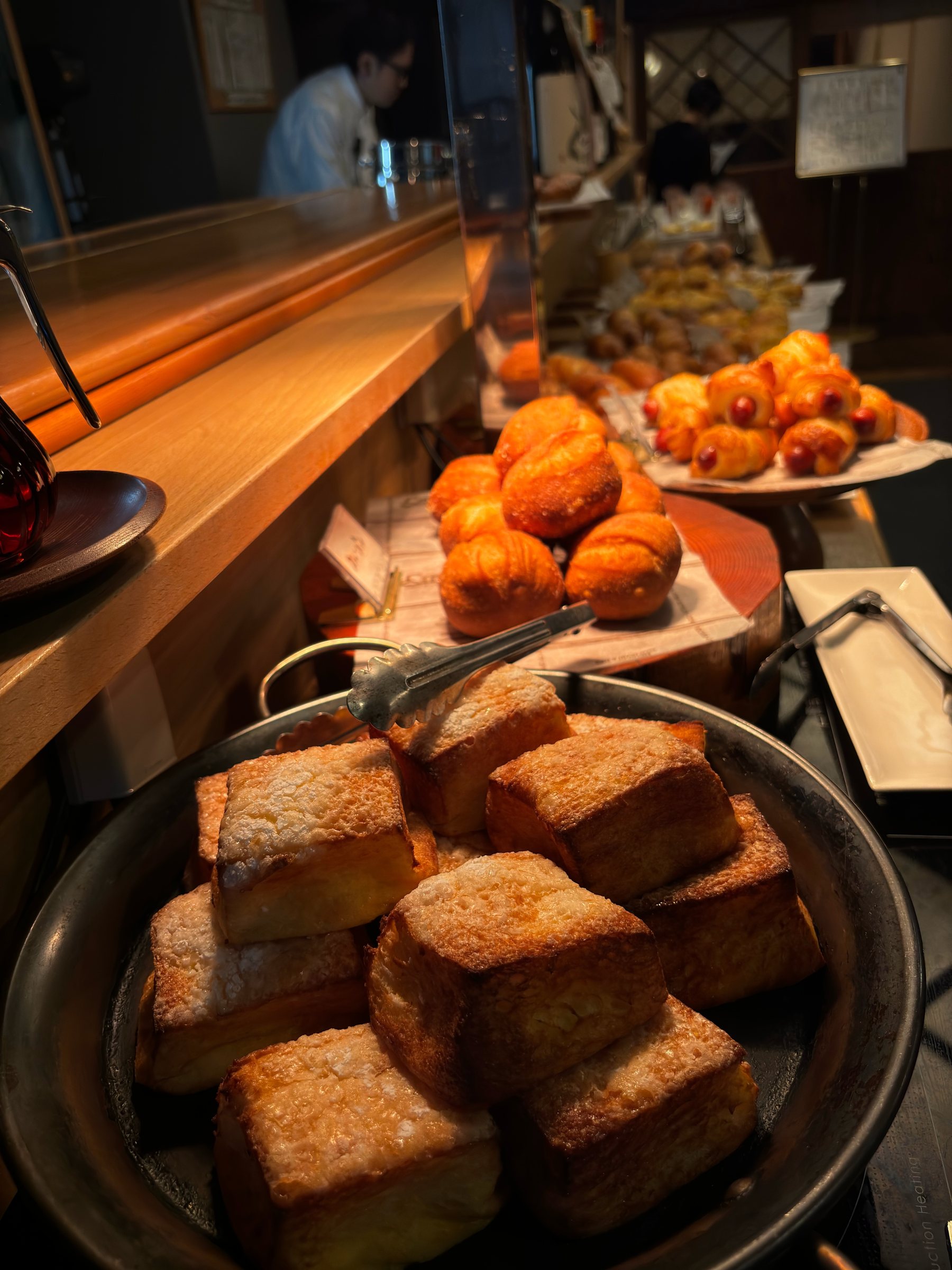Thick slices of fried bread in a pan, with more baked goods behind.