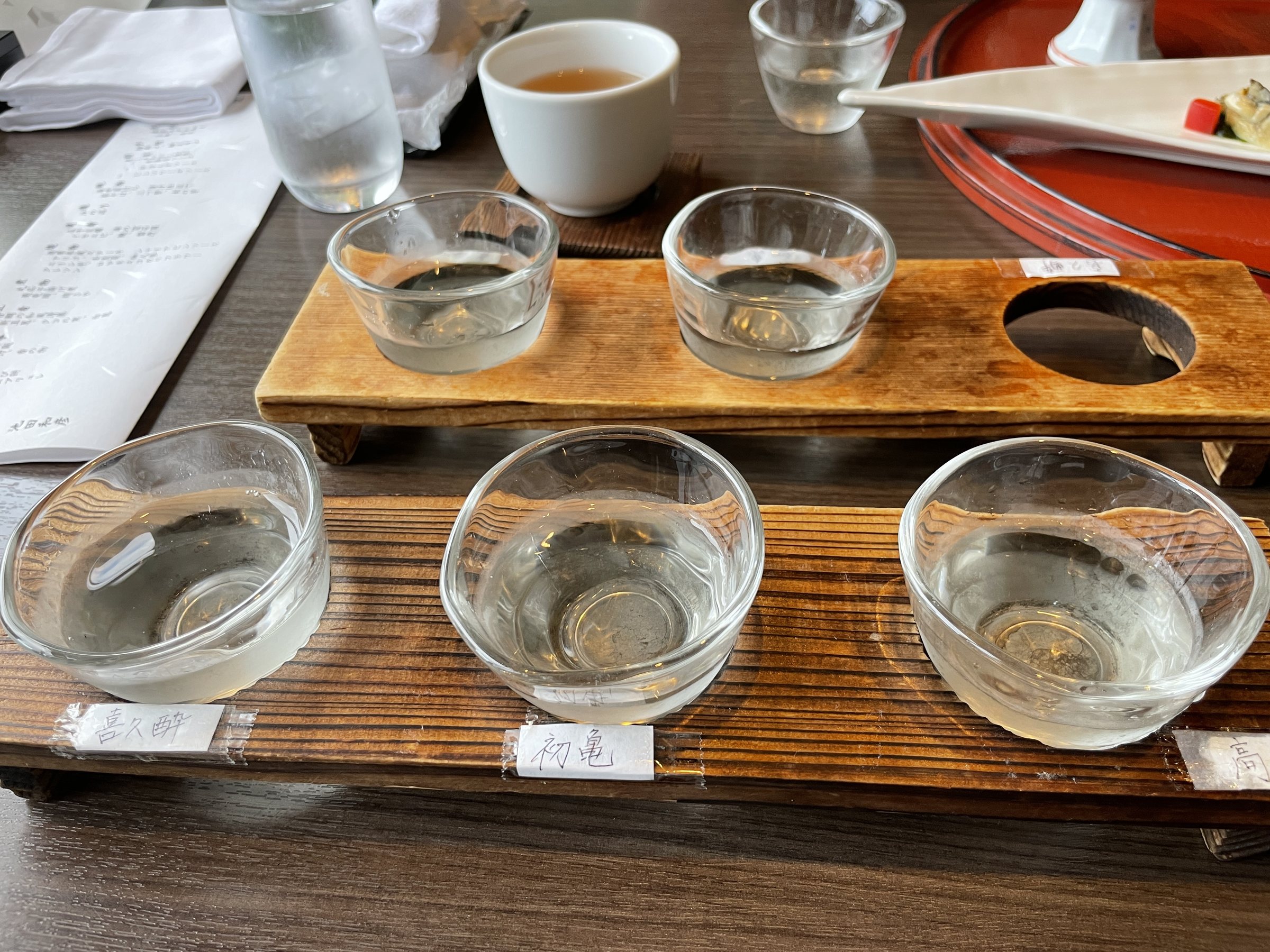 A tasting flight of local sake in small glasses on a wooden board.
