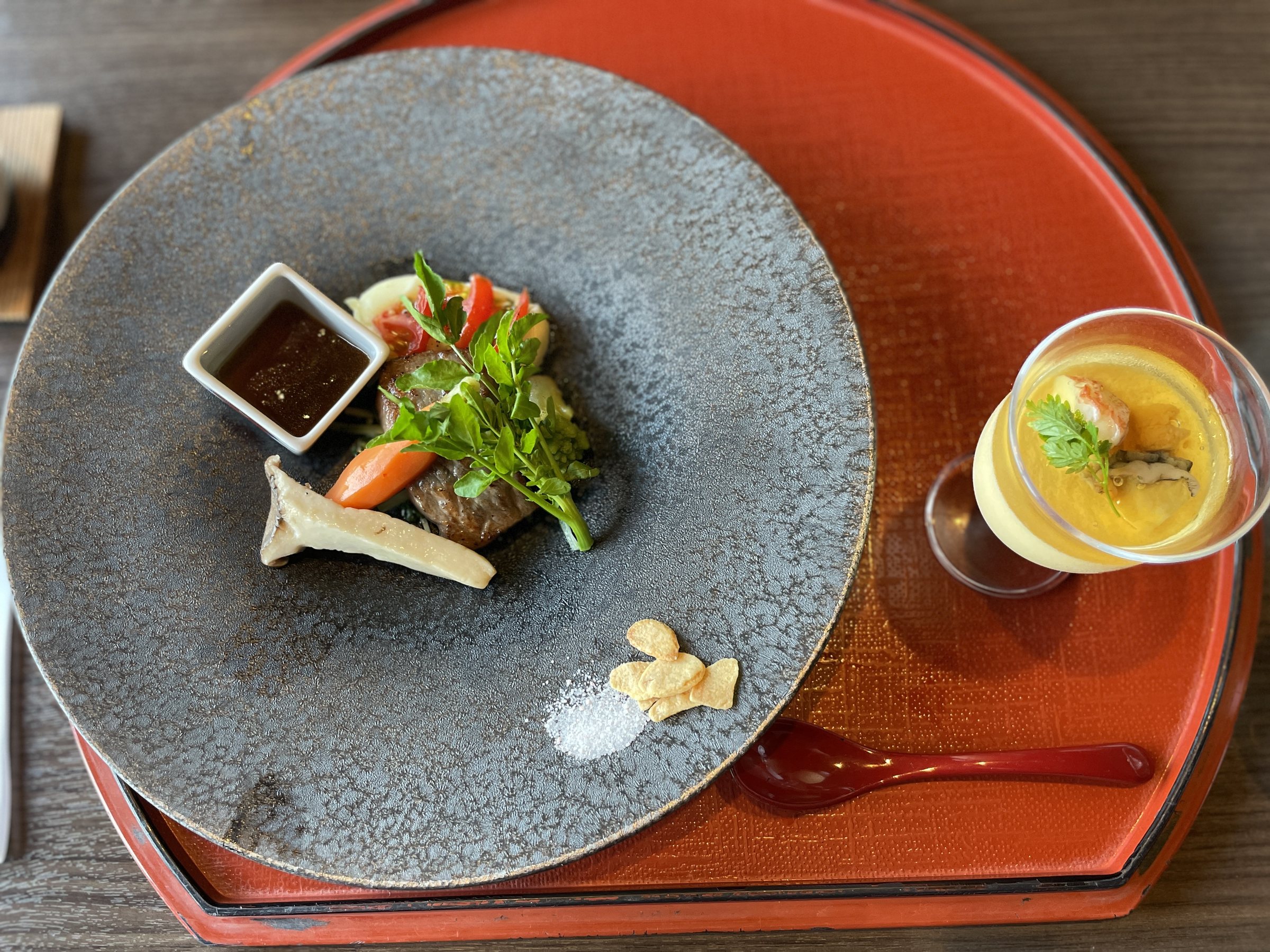 Beef steak on a gray plate, with a small glass of chilled egg custard alongside.