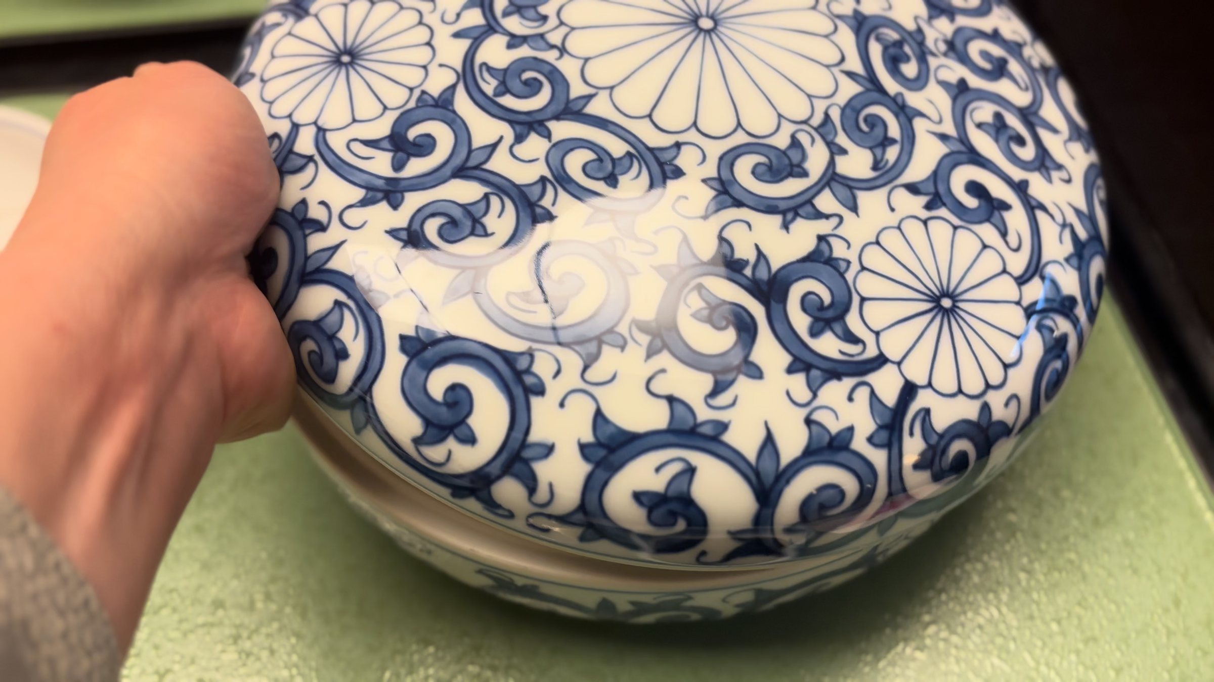 A lidded blue-and-white porcelain bowl, held up to the camera.