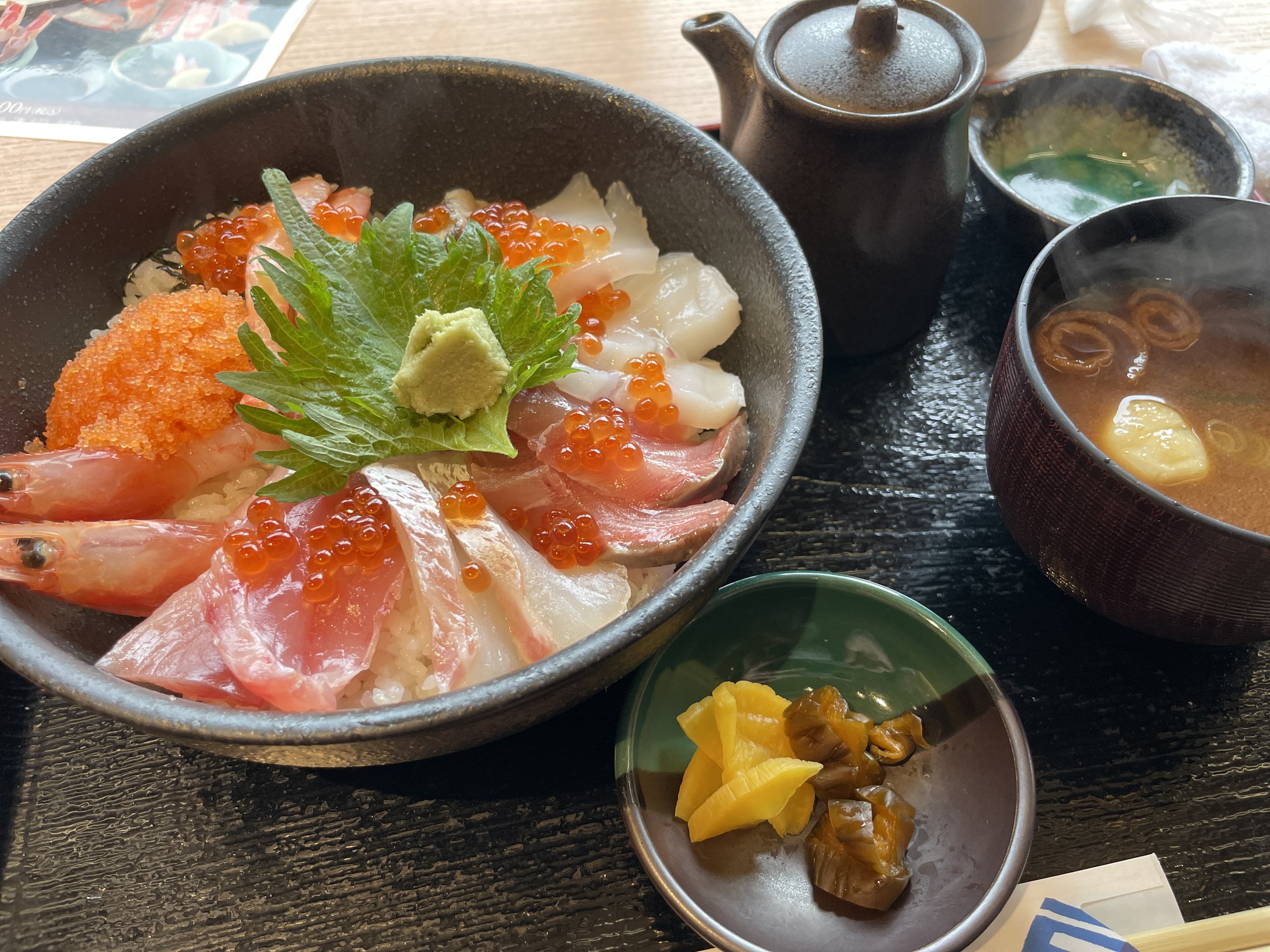 A seafood rice bowl topped with salmon roe, prawn and sashimi, with miso soup.