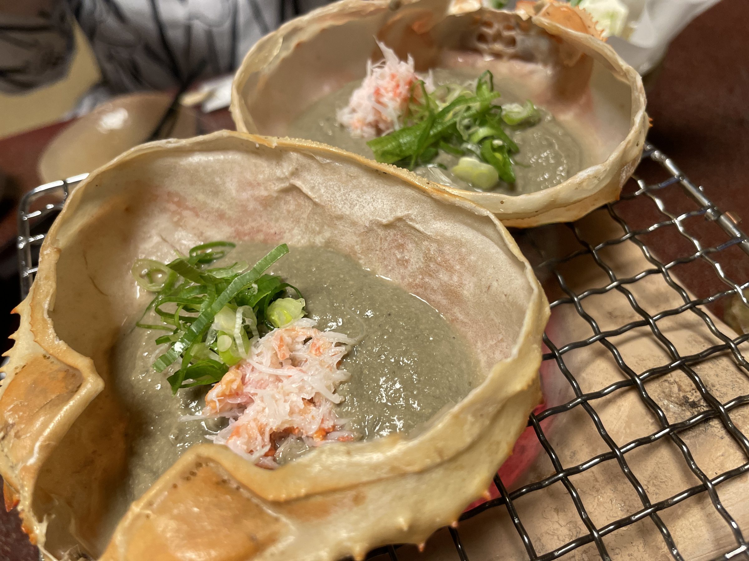 Crab shells filled with crab miso, warming on a grill.