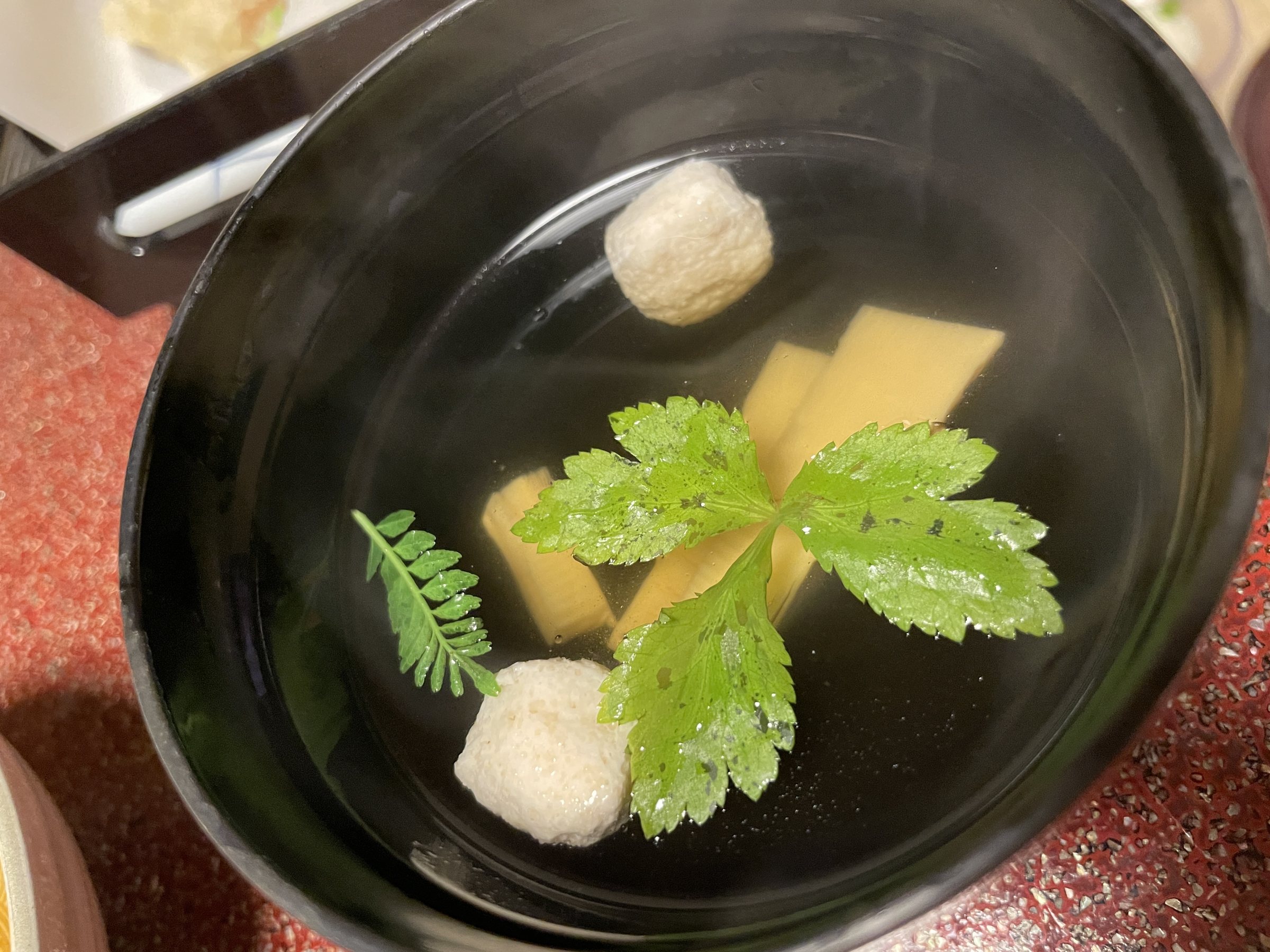 A clear soup with small dumplings and a sprig of greenery.