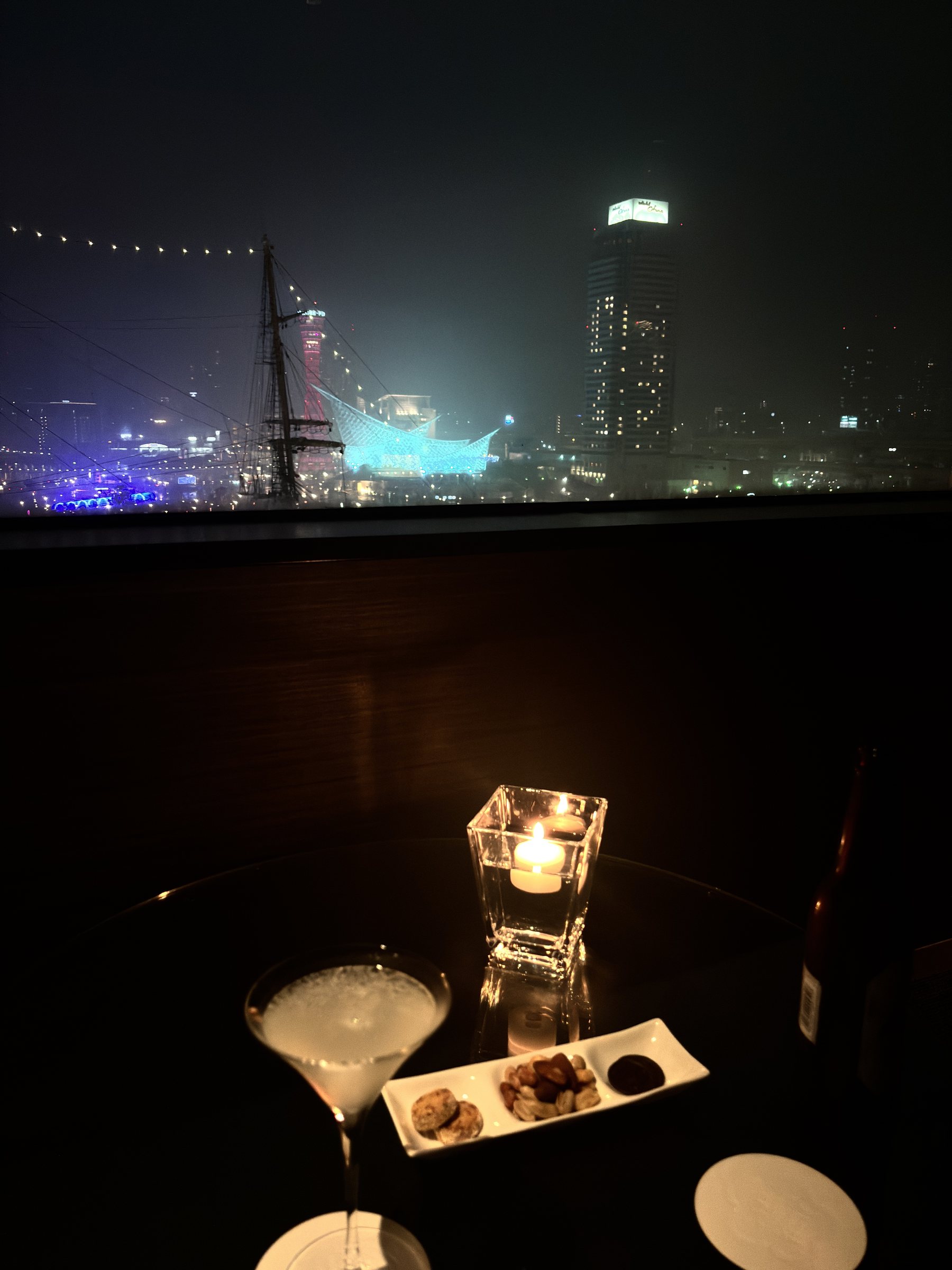 A cocktail by candlelight, with the harbor lights behind.