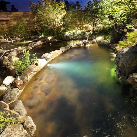 A rock-edged pool lit from beneath at night. (Photo: Kobe Minato Onsen Ren official website)
