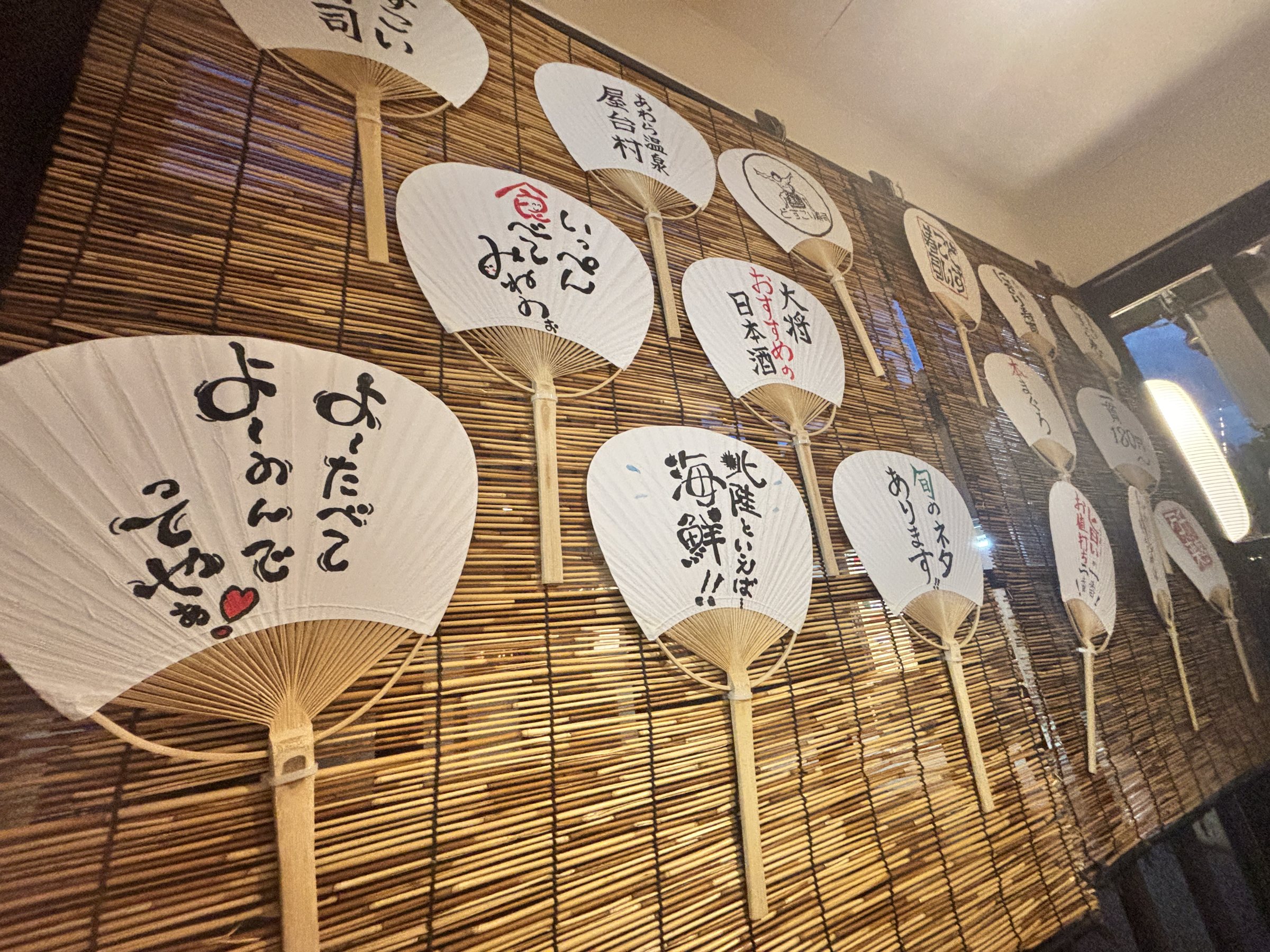 Paper fans with handwritten slogans on a bamboo screen.