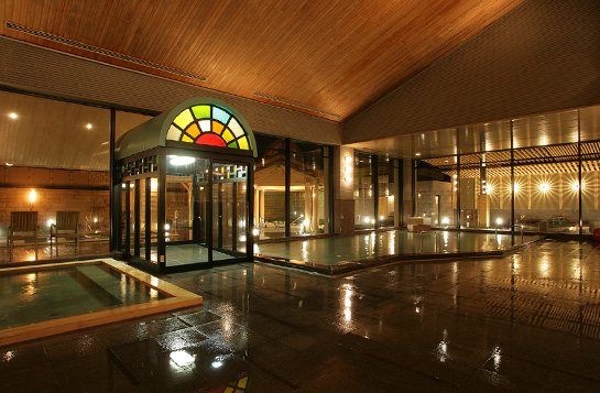 The large indoor bath at night, beneath a stained-glass window (photo from the ryokan’s official website).