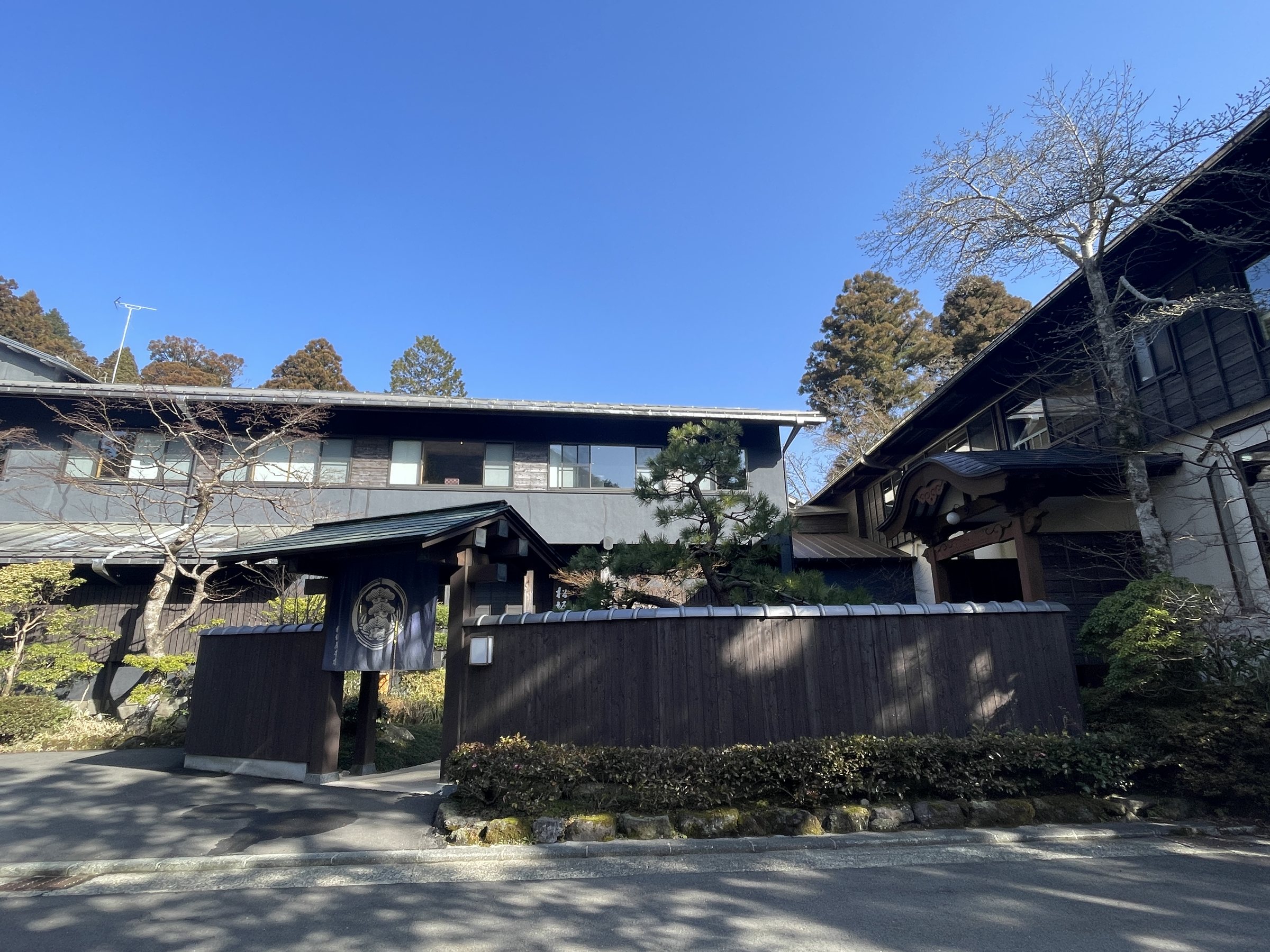 The entrance gate and low walls of the ryokan, with the hills of Hakone behind.