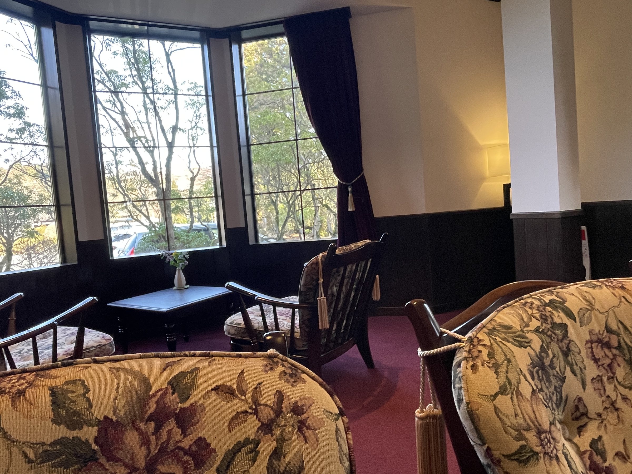 A bay window in the lobby lounge, with floral armchairs and lace-curtained light.